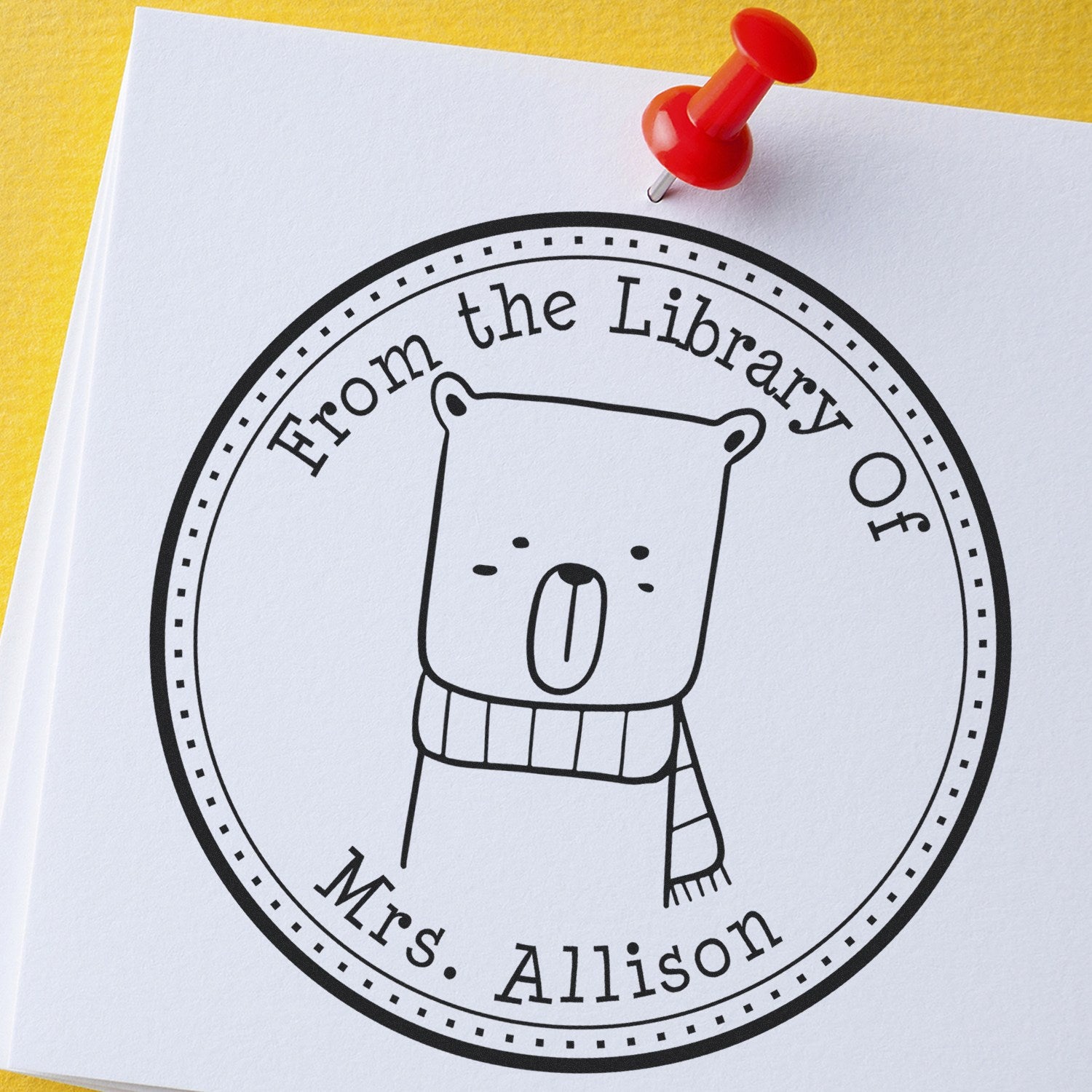 BounceTail Cartoon Animal Self-Inking Custom-Made Ex Libris Stamp featuring a cute bear with a scarf, labeled "From the Library Of Mrs. Allison," on white paper. A red pushpin secures the paper on a yellow background. Custom New Address Stamper concept.