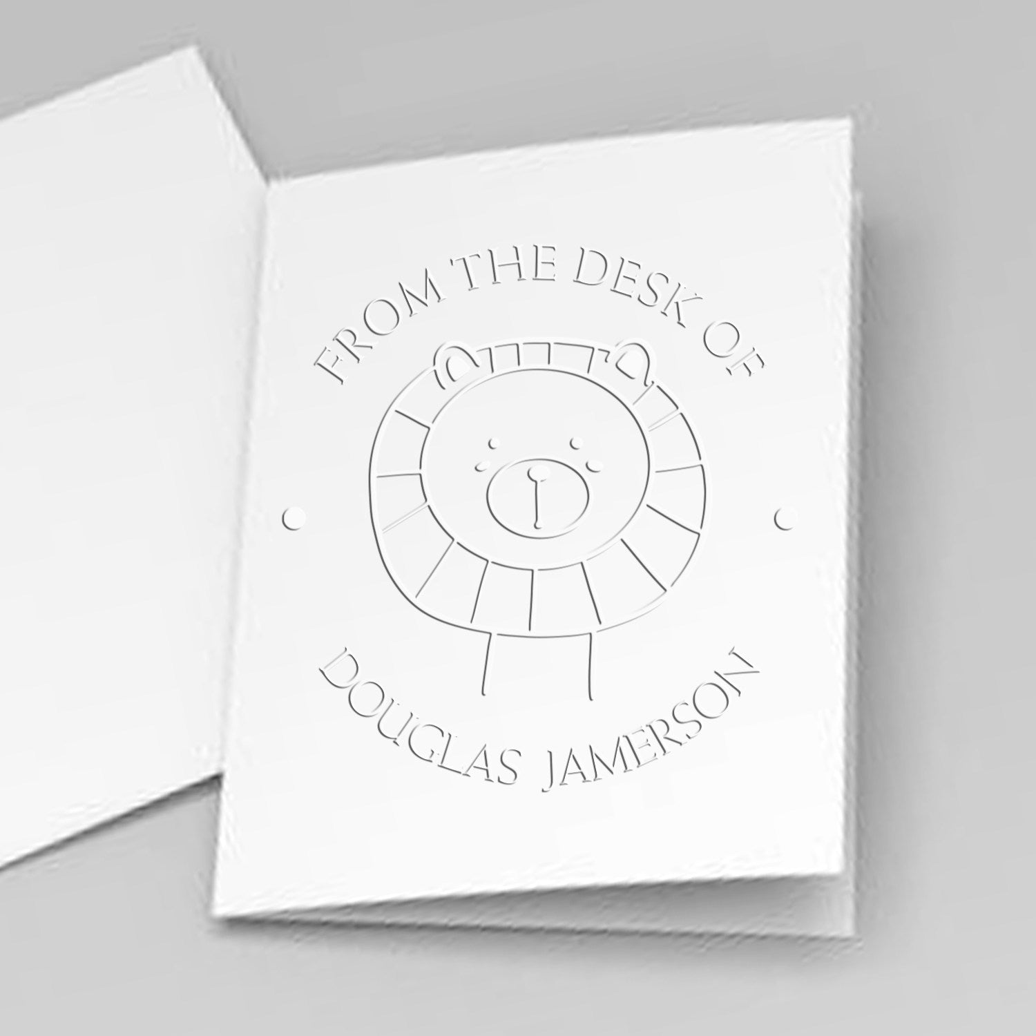 Image of a white card embossed with a FlutterPaws cartoon animal hybrid design, featuring a lion. The text reads "From the Desk of Douglas Jamerson." This customized library ownership embosser doubles as a customizable address stamper.