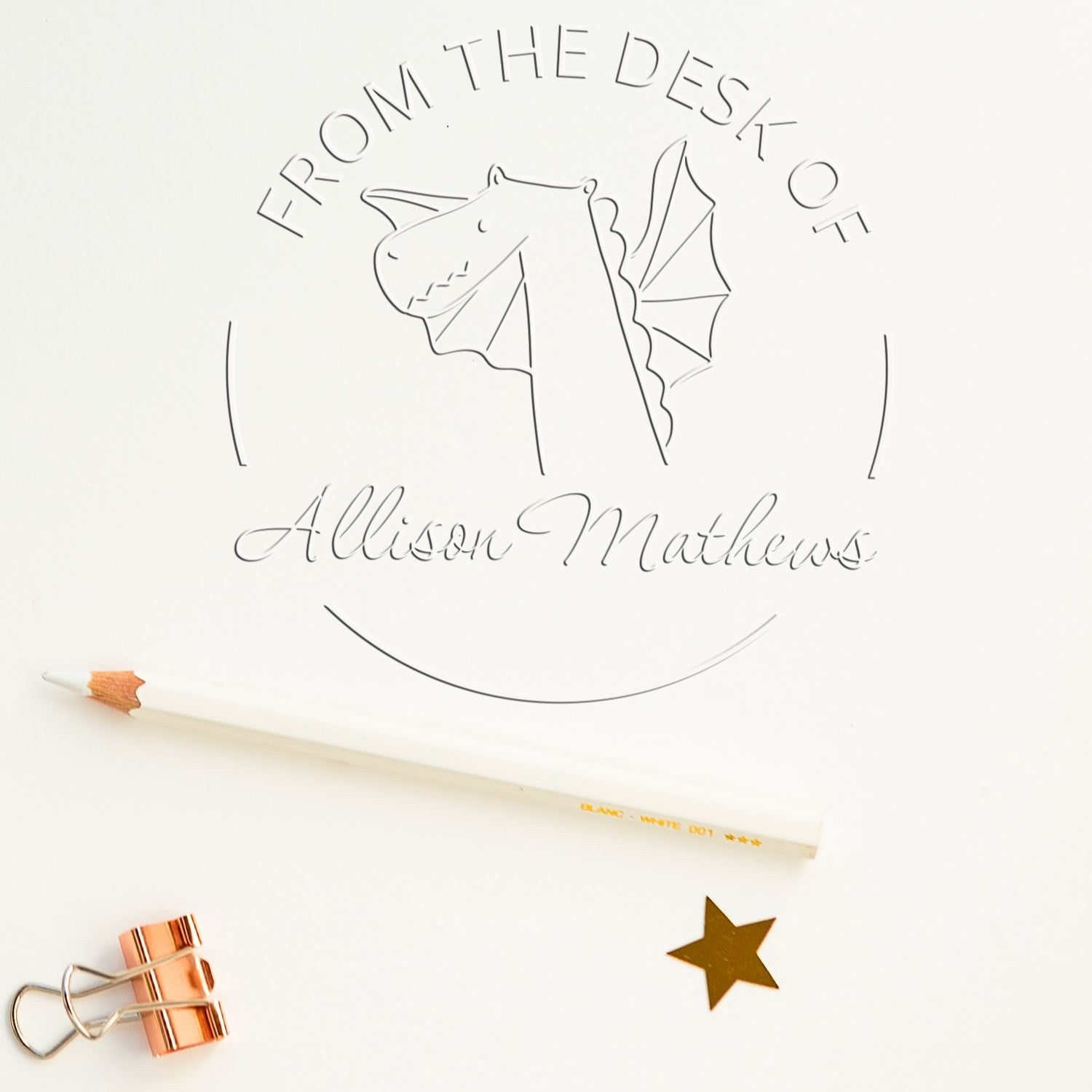 A SnuggleSnout cartoon animal design is featured on a personalized library seal with the name "Allison Mathews." The custom-made home stamper is shown in use, with a pencil, gold star, and paper clip nearby.