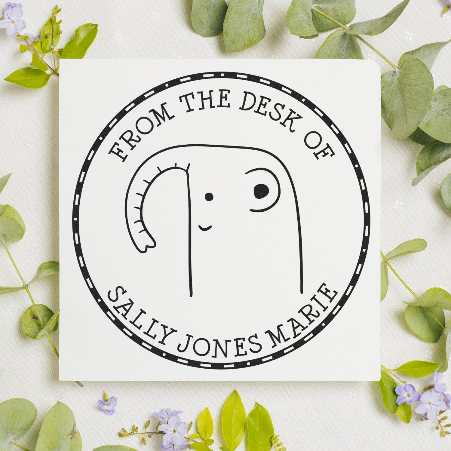 GiggleWiggle Cartoon Animal Pre-Inked Customizable Stamp from the Collection of Stamp, featuring a cute elephant design. This Customizable New Address Stamper is shown on a white card surrounded by green leaves and small purple flowers.