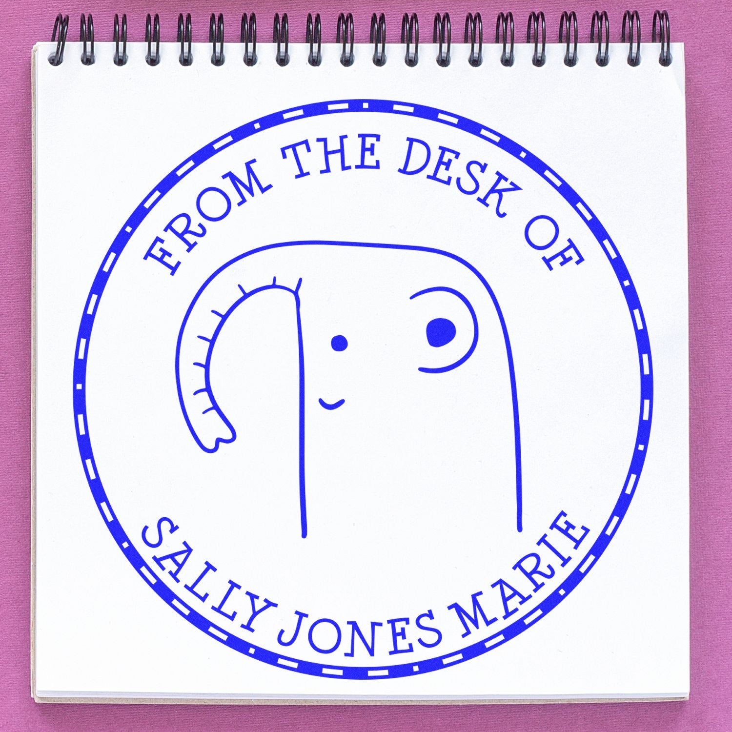 A cartoon animal with a wood handle, resembling a GiggleWiggle, is stamped on a notepad. The stamp reads "From the Desk of Sally Jones Marie" and is part of a personalized library of stamps. It's a customized new address stamp.