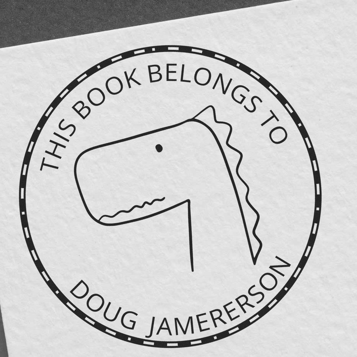 JellyBeanJump Cartoon Animal Pre-Inked Customizable Library Stamp featuring a simple dinosaur design with text "This Book Belongs To Doug Jamerson." Ideal as a Customizable Mailing Stamp for personalizing books or letters.