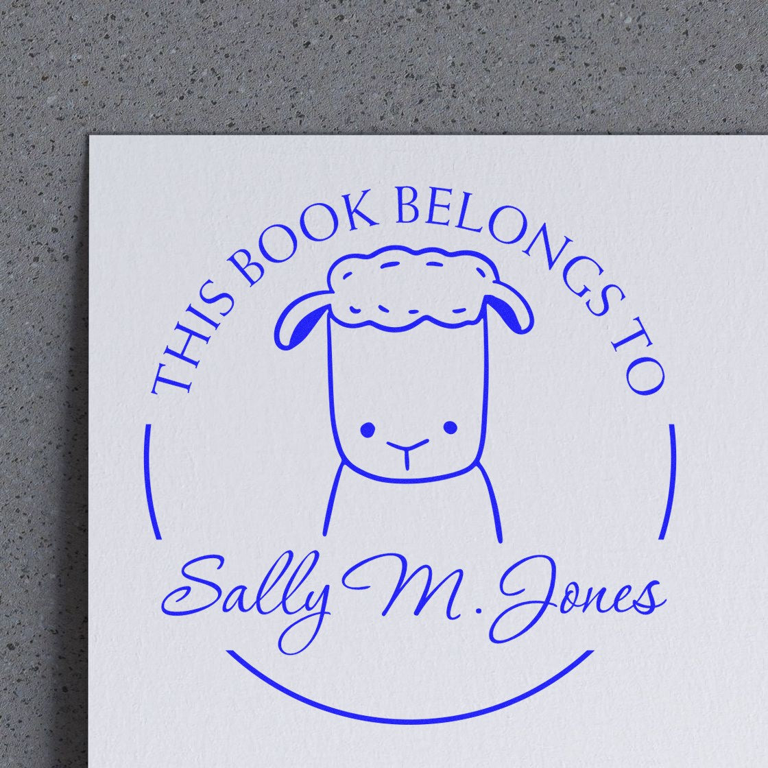 Image of a custom-made new address stamper featuring a wood handle TwirlTail cartoon animal design. The stamp reads "This Book Belongs To" with a sheep illustration and the name "Sally M. Jones," customized from the library of stamp collection.