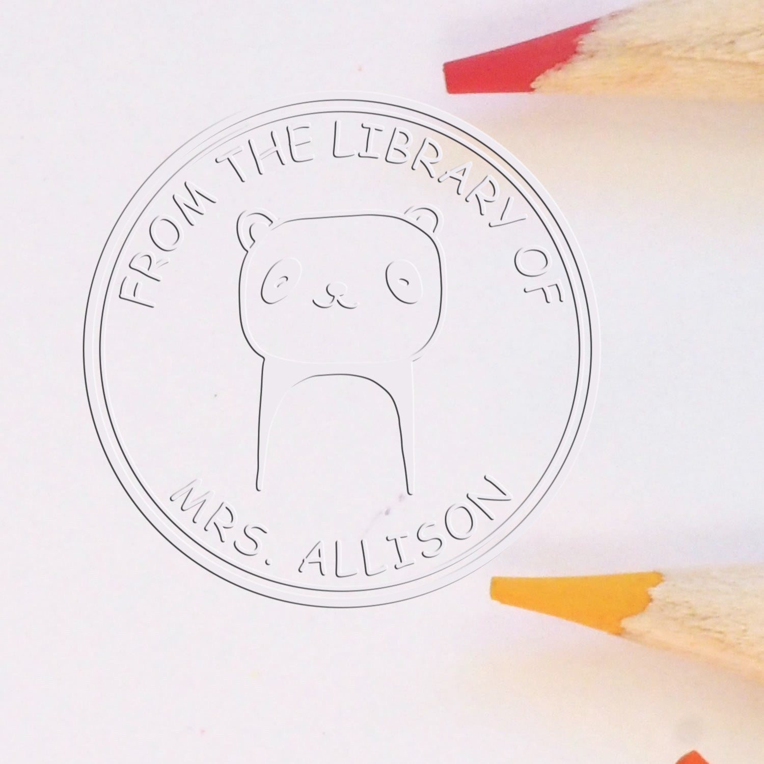 Soft TumbleTuft cartoon animal custom-made book logo seal featuring a cute animal design with the text "From the Library of Mrs. Allison." The seal is used with a custom home stamper, surrounded by colored pencils on a white background.