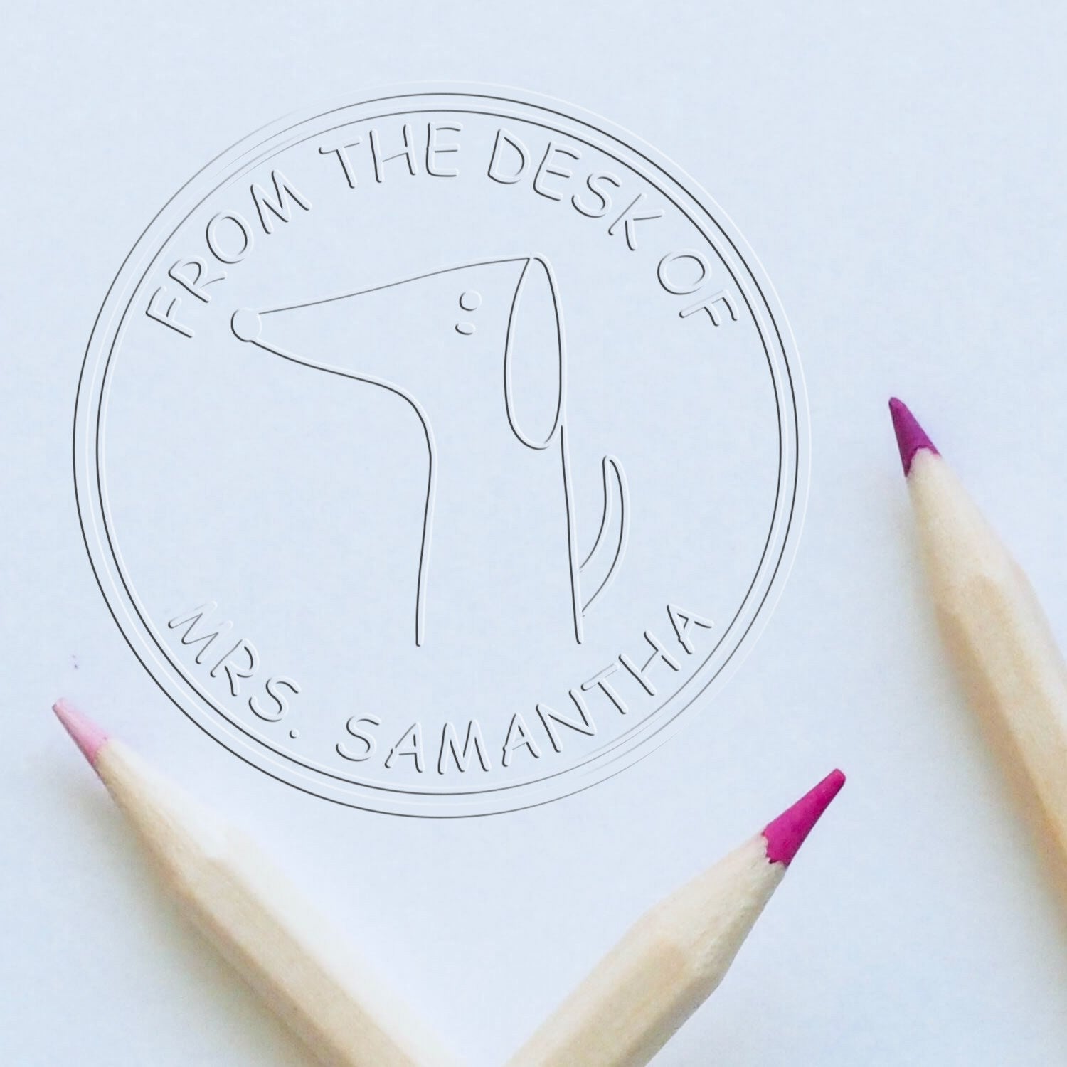 Soft WiggleWag cartoon animal custom-made book identity embosser featuring a simple dog design with "From the Desk of Mrs. Samantha" text. Surrounded by three colored pencils, it also functions as an address stamp.