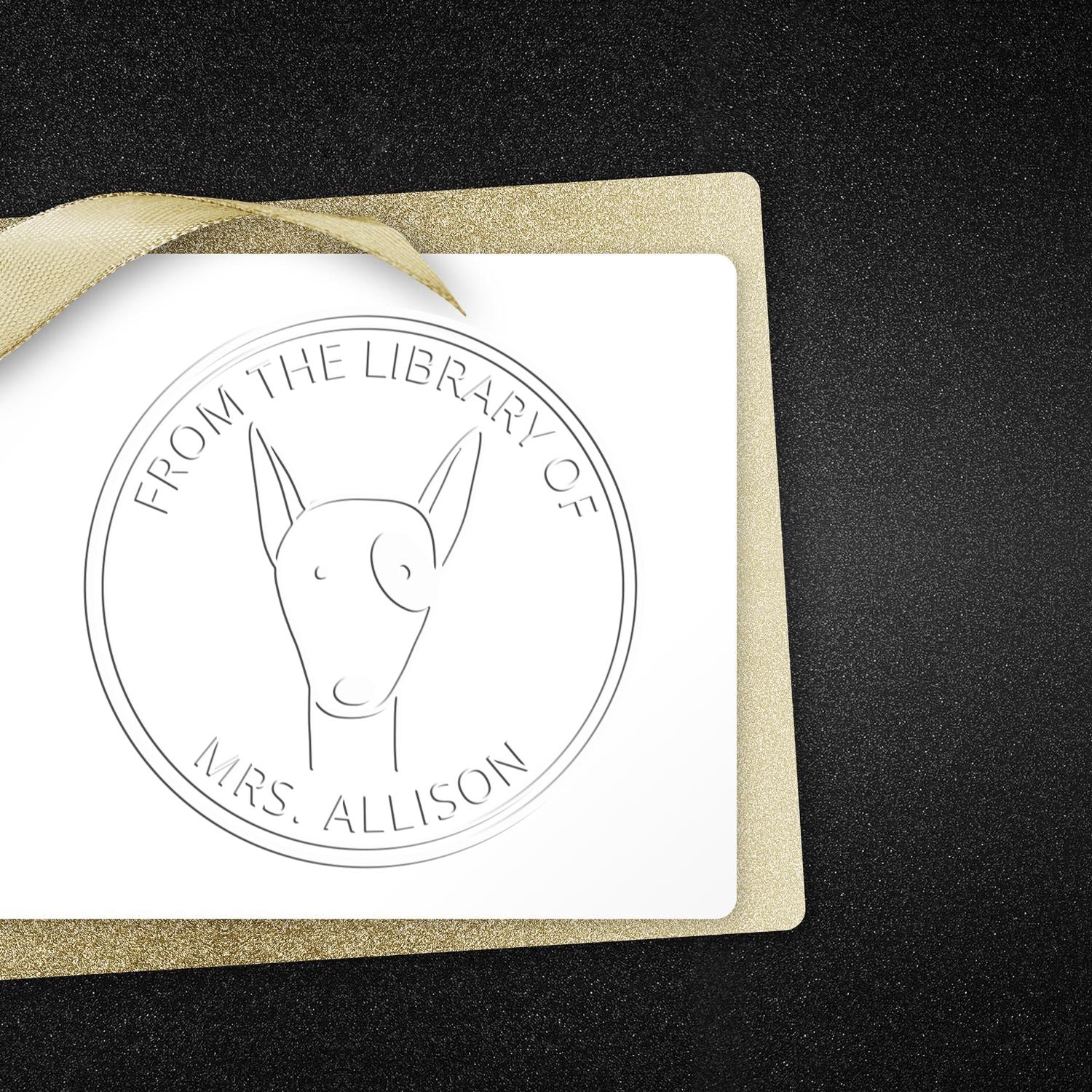 RuffleRump cartoon animal embossing seal on a white card with "From the Library of Mrs. Allison" text. The seal is a personalized book lover gift. A gold envelope is partially visible. Personalizable mailing stamper concept.