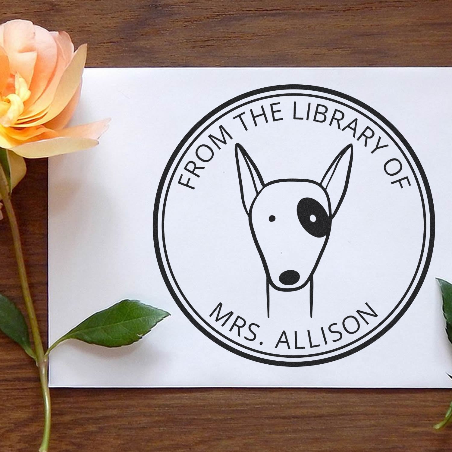 RuffleRump Cartoon Animal Self-Inking Personalizable From The Library Of Stamp featuring a cute dog design on a white paper. Personalized Home Stamper with "From the Library of Mrs. Allison" text, surrounded by a rose and leaves on a wooden surface.