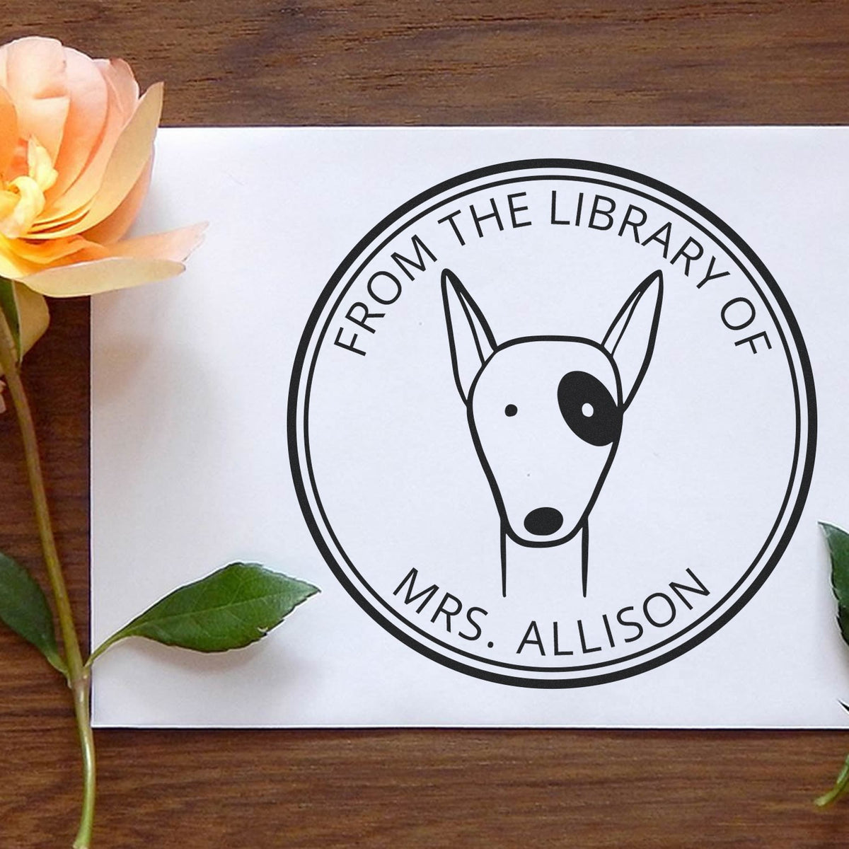Slim Pre-Inked RuffleRump Cartoon Animal Custom Book Library Stamp featuring a customizable address stamper design with a cute dog illustration, placed on a white envelope surrounded by a rose and green leaves on a wooden surface.