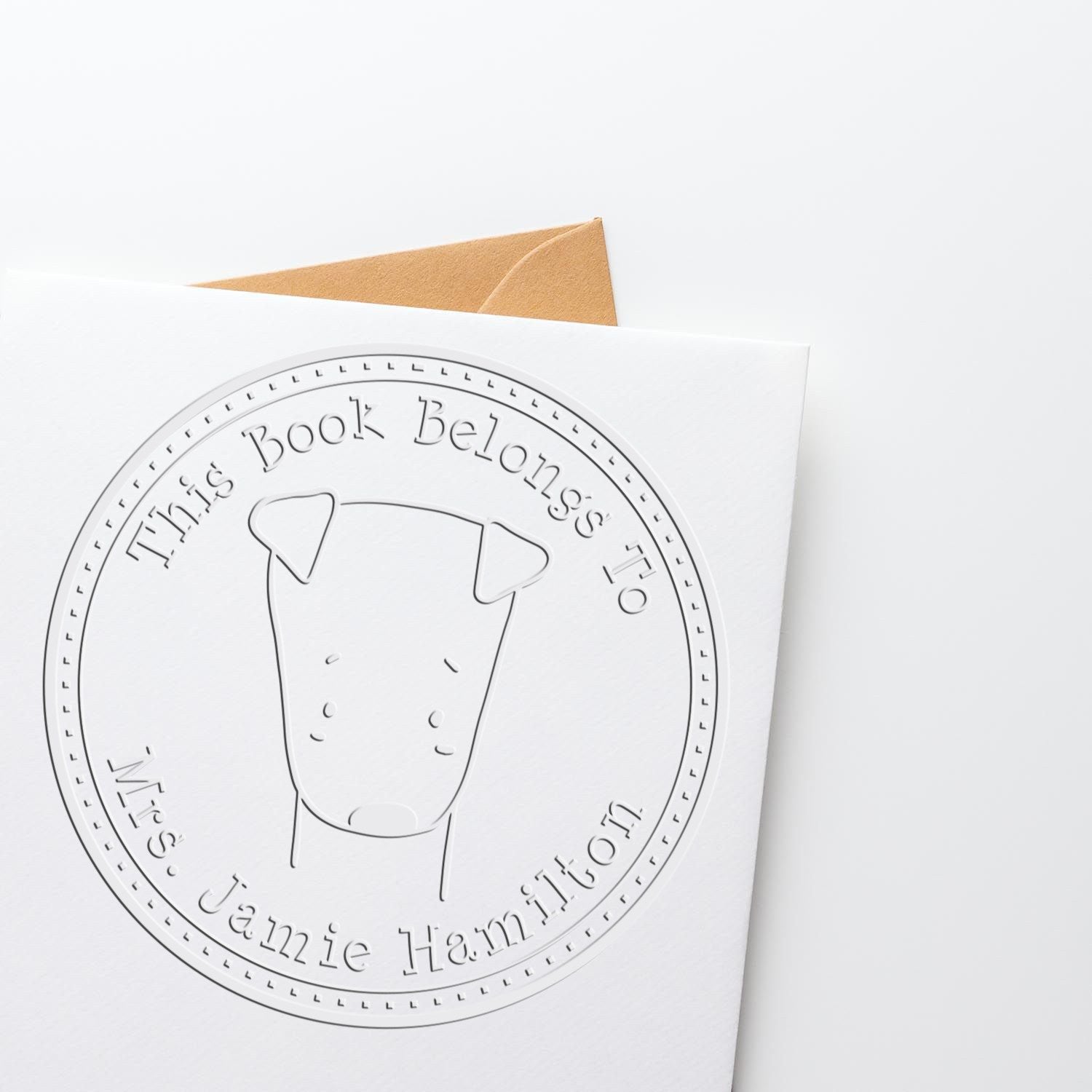 A custom-made book identity embossing seal featuring a Soft SizzleSniff cartoon animal design is shown on a white card. The text reads "This Book Belongs To Mrs. Jamie Hamilton." A customizable return mail stamp is partially visible in the background.
