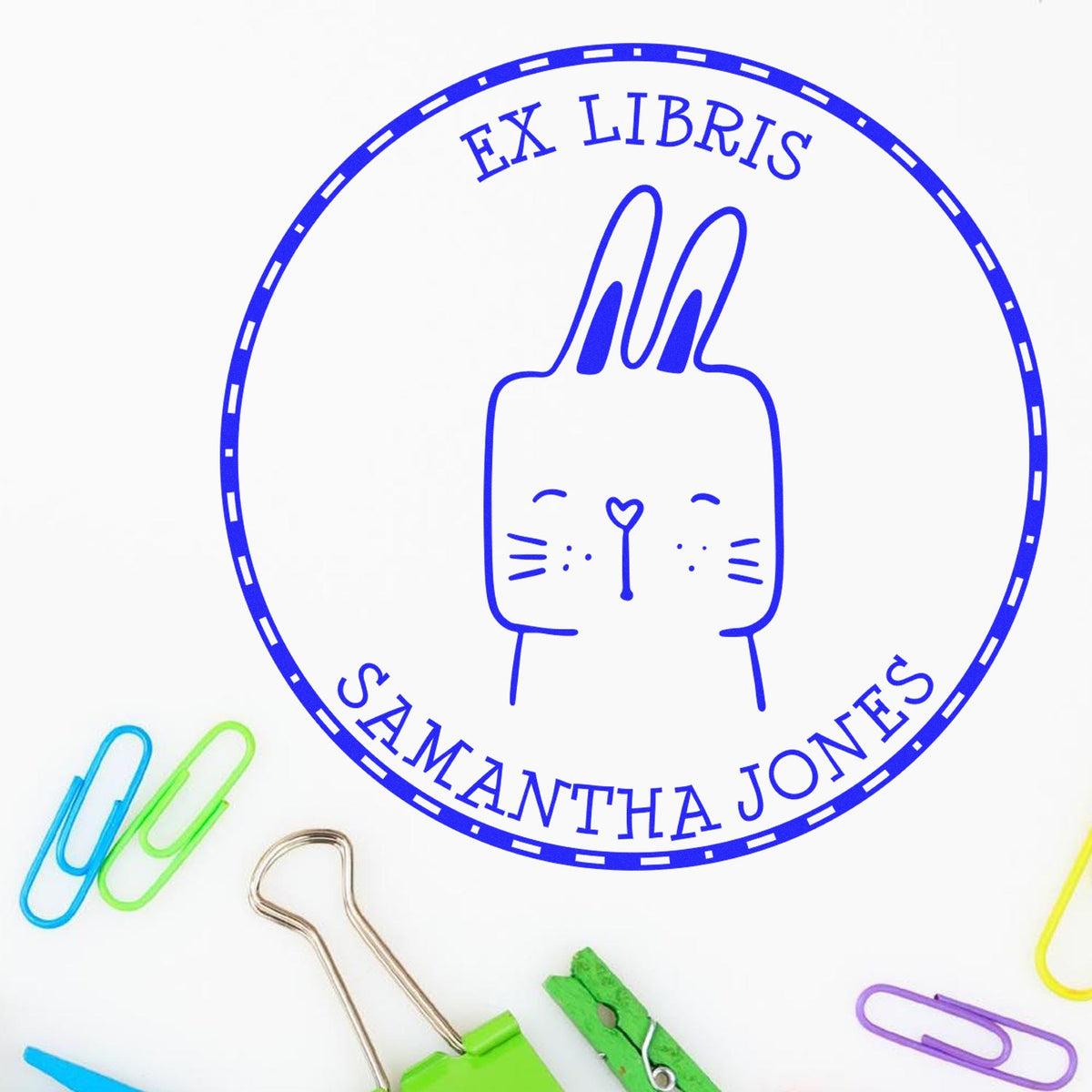 Slim Pre-Inked SquirmSquiggle Cartoon Animal Custom Book Library Name Stamp featuring a cute rabbit design with "Ex Libris" and "Samantha Jones" text. Surrounded by colorful paper clips and a binder clip, showcasing a Customized Home Stamp.