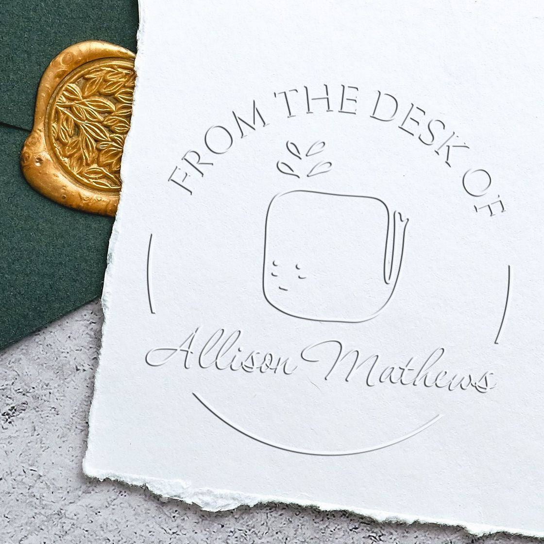 Image of a WhiffleWhirl cartoon animal embossed on paper with the text "From the Desk of Allison Mathews." The handheld personalized library embosser creates a custom mailing stamp. A gold wax seal is partially visible on a green envelope.
