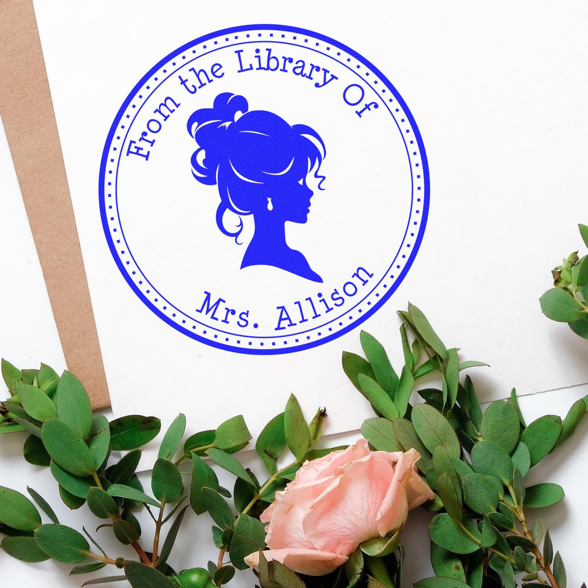 Blue circular library stamp seal with woman silhouette and From the Library of Mrs. Allison, on white paper with greenery and pink rose.