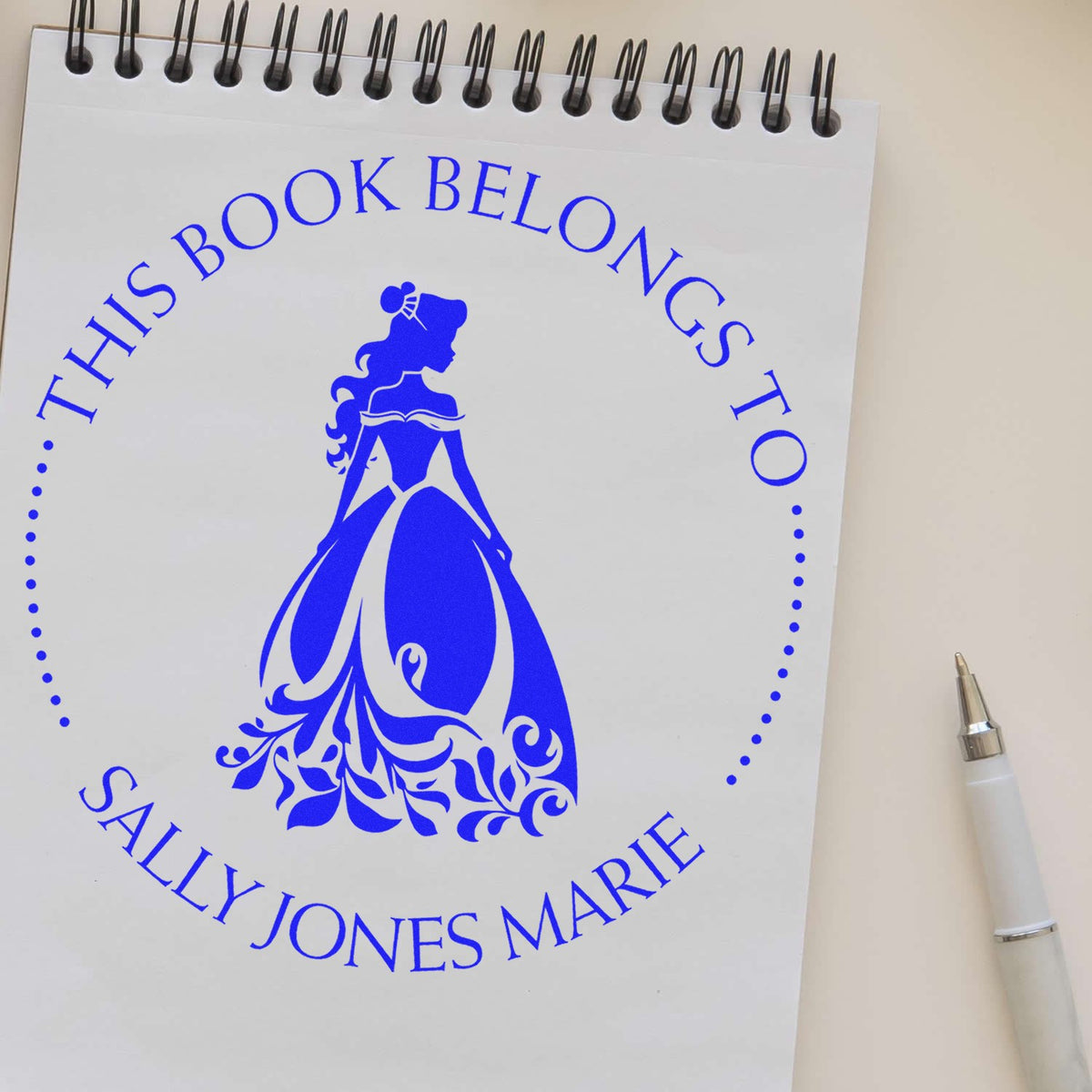 Blue custom stamp and seal reading This book belongs to Sally Jones Marie with princess silhouette on spiral notebook, white pen.