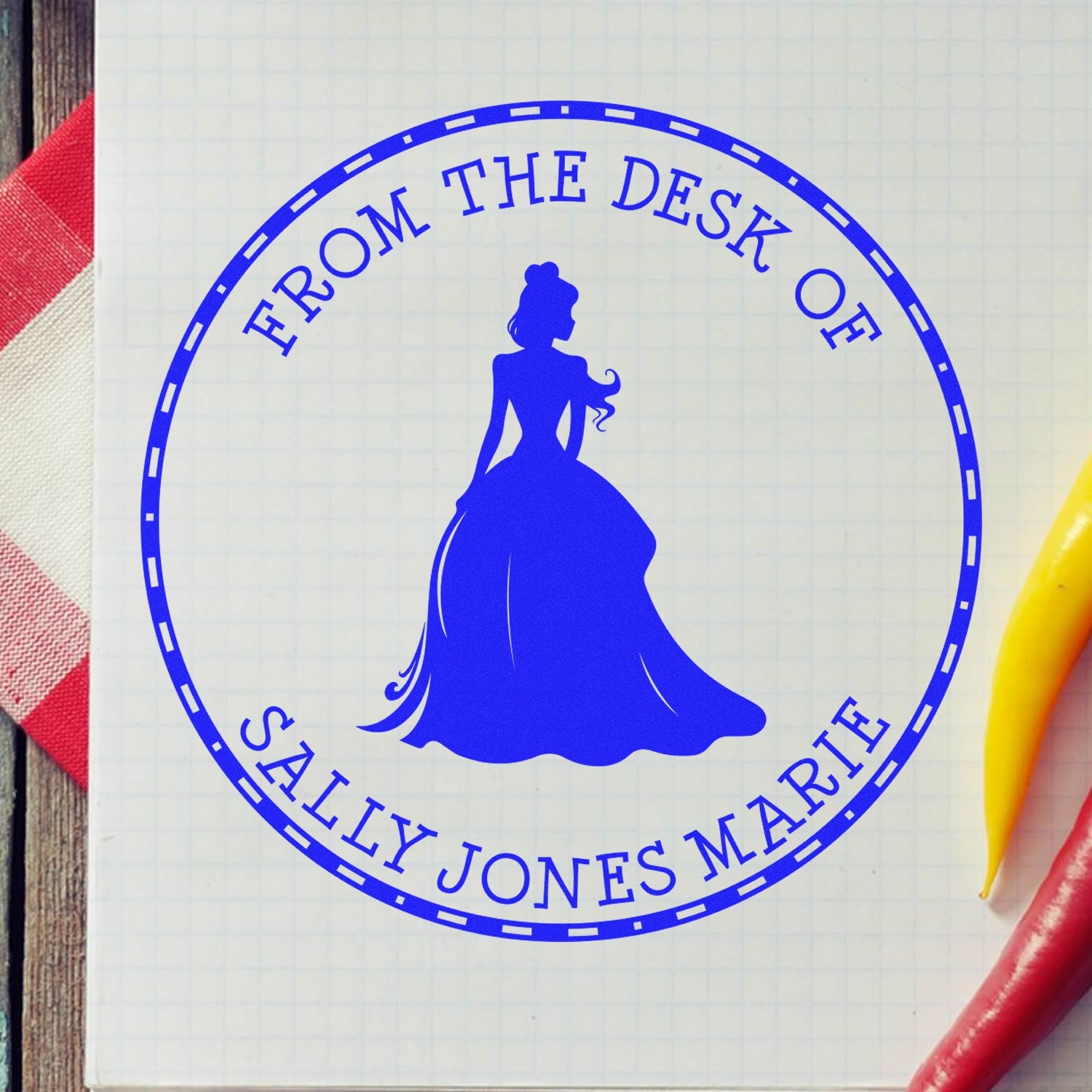 Blue custom stamp seal with queen silhouette and From the Desk of Sally Jones Marie on graph paper, with red and yellow pens.