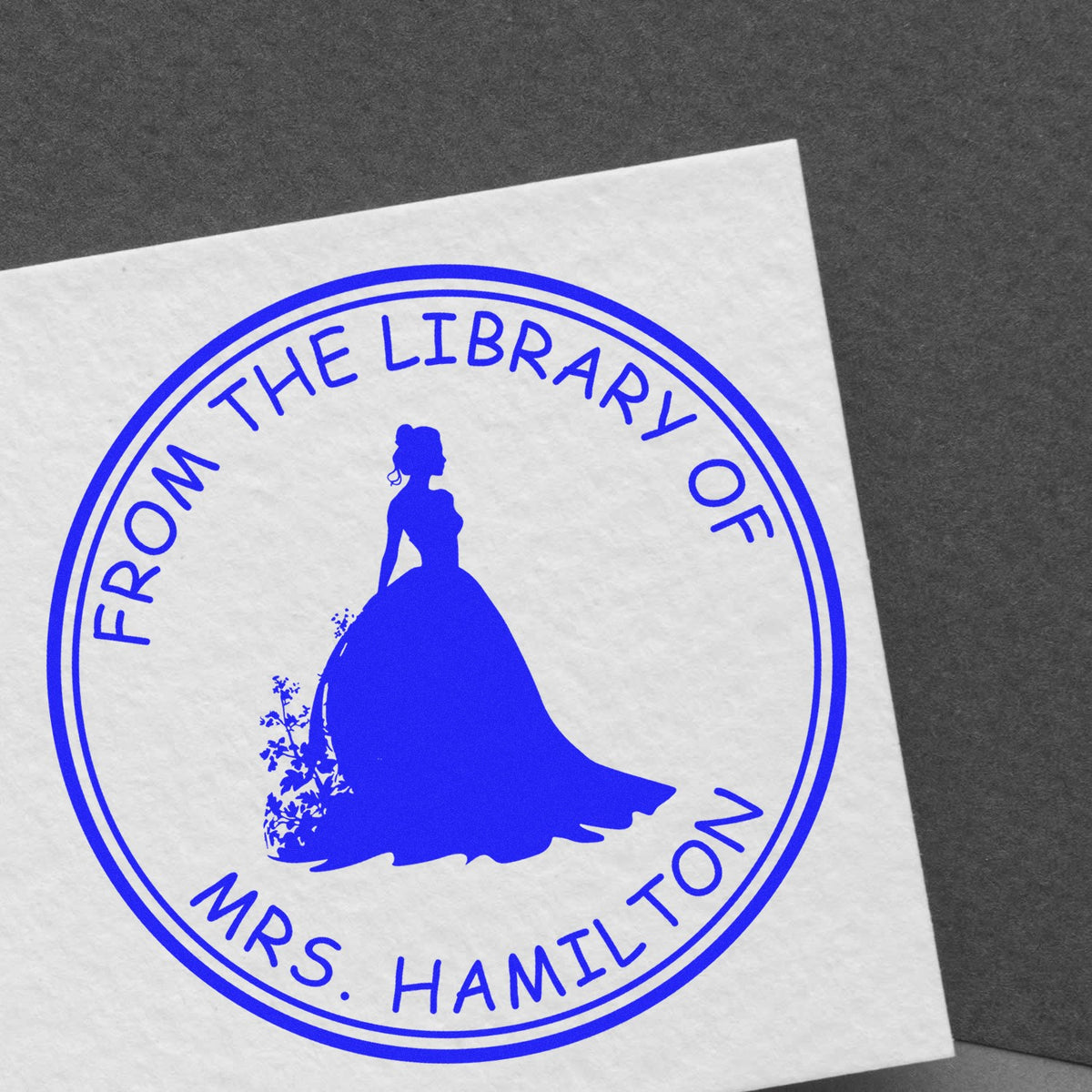 Blue circular book stamp seal on white paper with woman silhouette and From the Library of Mrs. Hamilton text.
