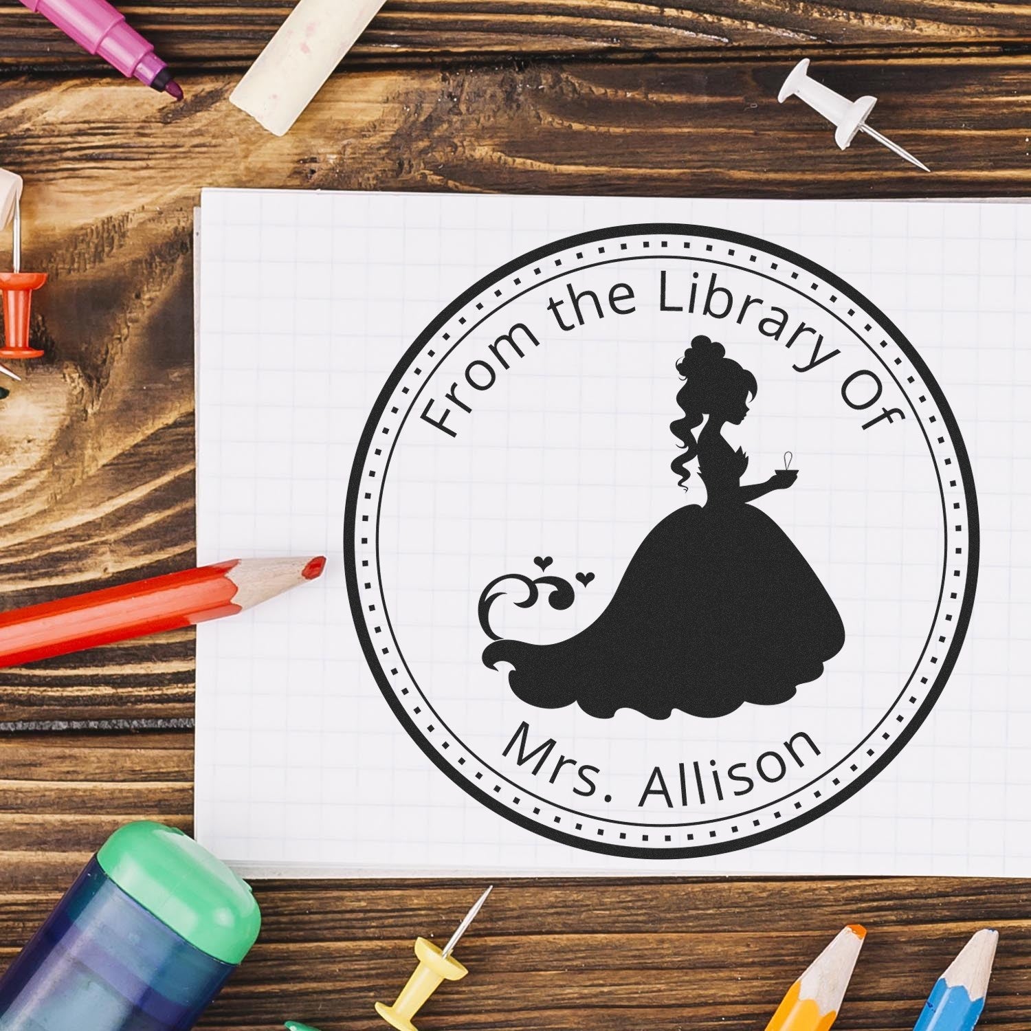 Black custom library seal stamp on white grid paper, with a woman silhouette and "From the Library Of Mrs. Allison" on a wooden desk.