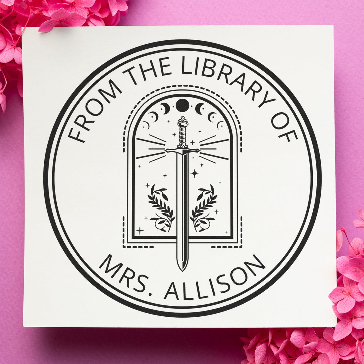 Black custom library stamp seal with sword and laurel, From the Library of Mrs. Allison, on white card with pink flowers.