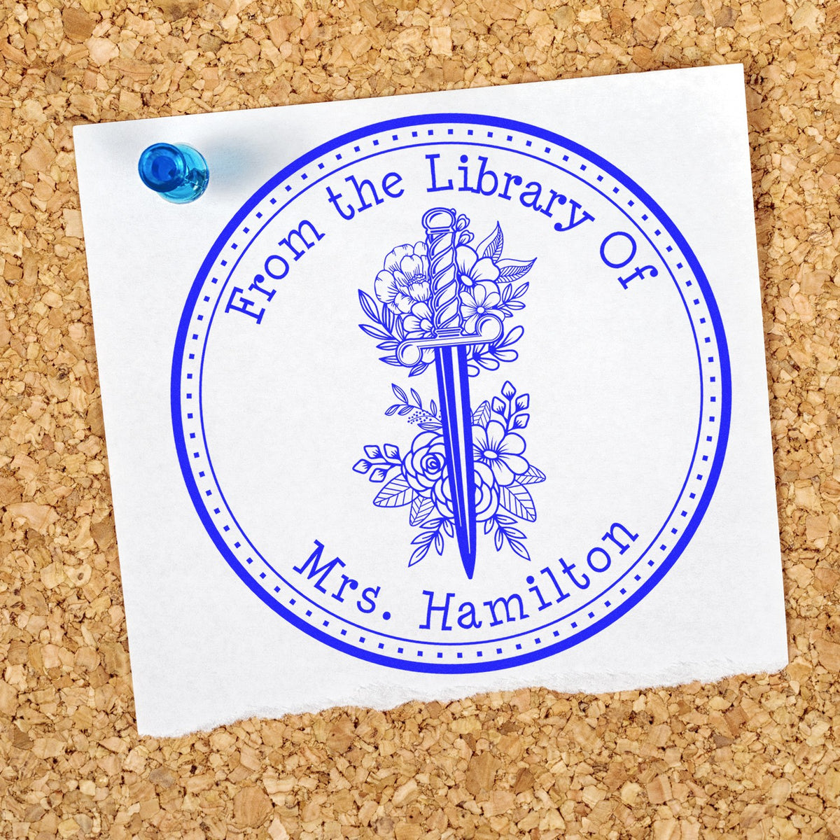 Blue circular library stamp seal with floral sword design and text for Mrs. Hamilton, pinned to corkboard.