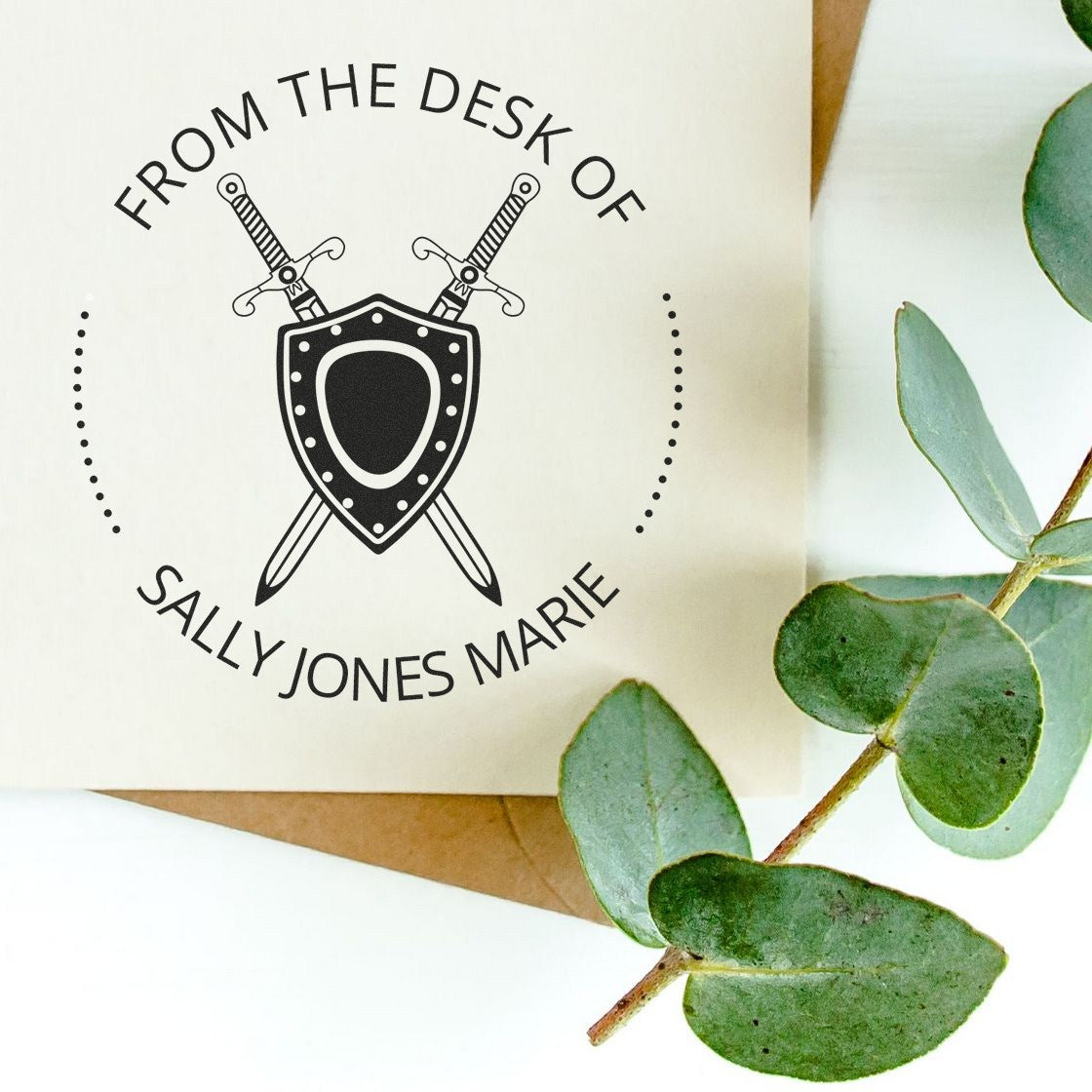 Personalized black stamp and seal crest with crossed swords on cream card, accented by green eucalyptus leaves.