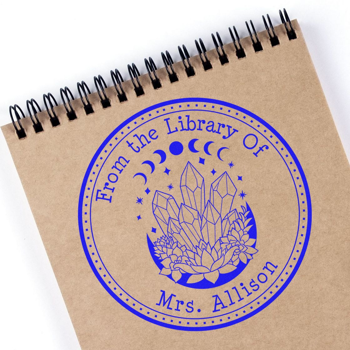 Blue circular library book stamp on kraft notebook, with crystals, flowers and moon phases, reading From the Library of Mrs. Allison.