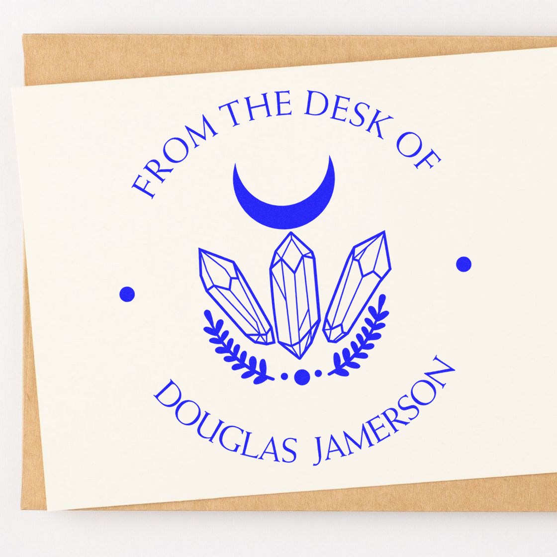 Blue custom desk stamp seal with crescent moon and crystal design on white card, over kraft paper.