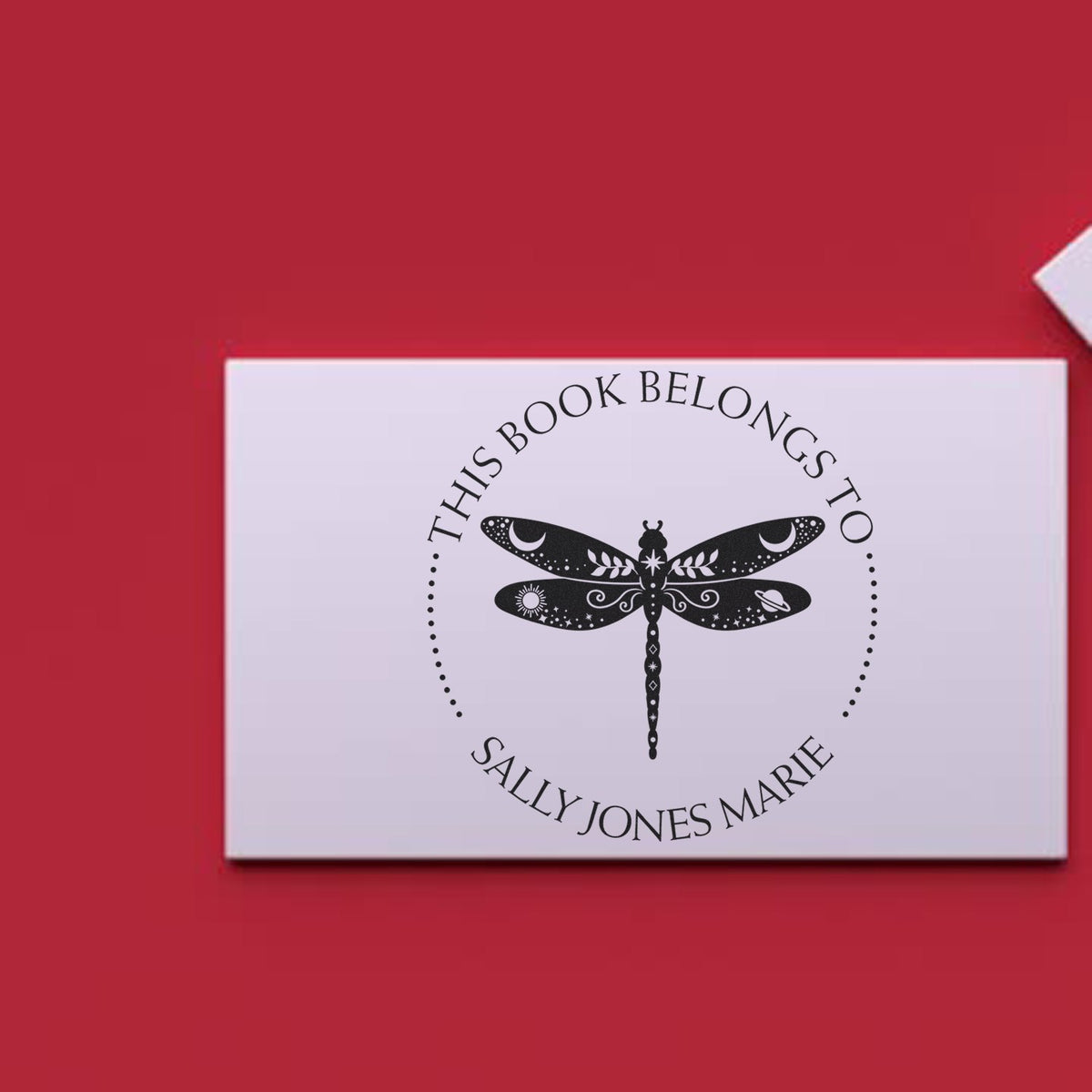 White custom book stamp and seal with black dragonfly and This Book Belongs to Sally Jones Marie on a red background.