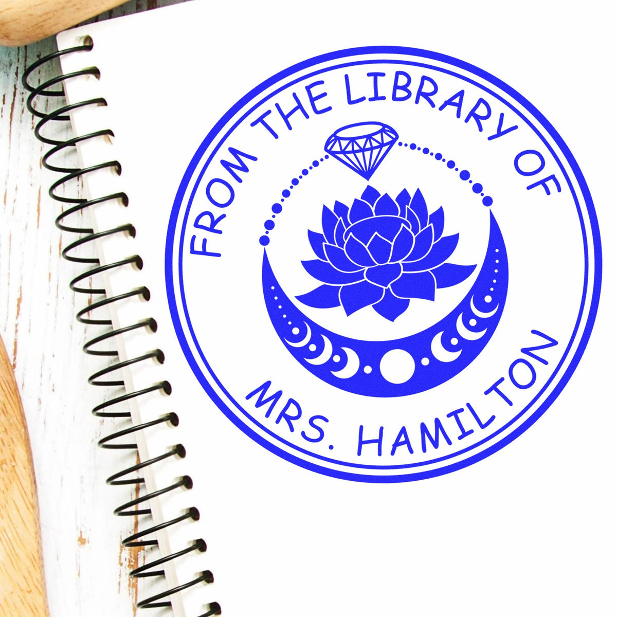 Blue circular library stamp seal with lotus and diamond, reading From the Library of Mrs. Hamilton on white notebook.