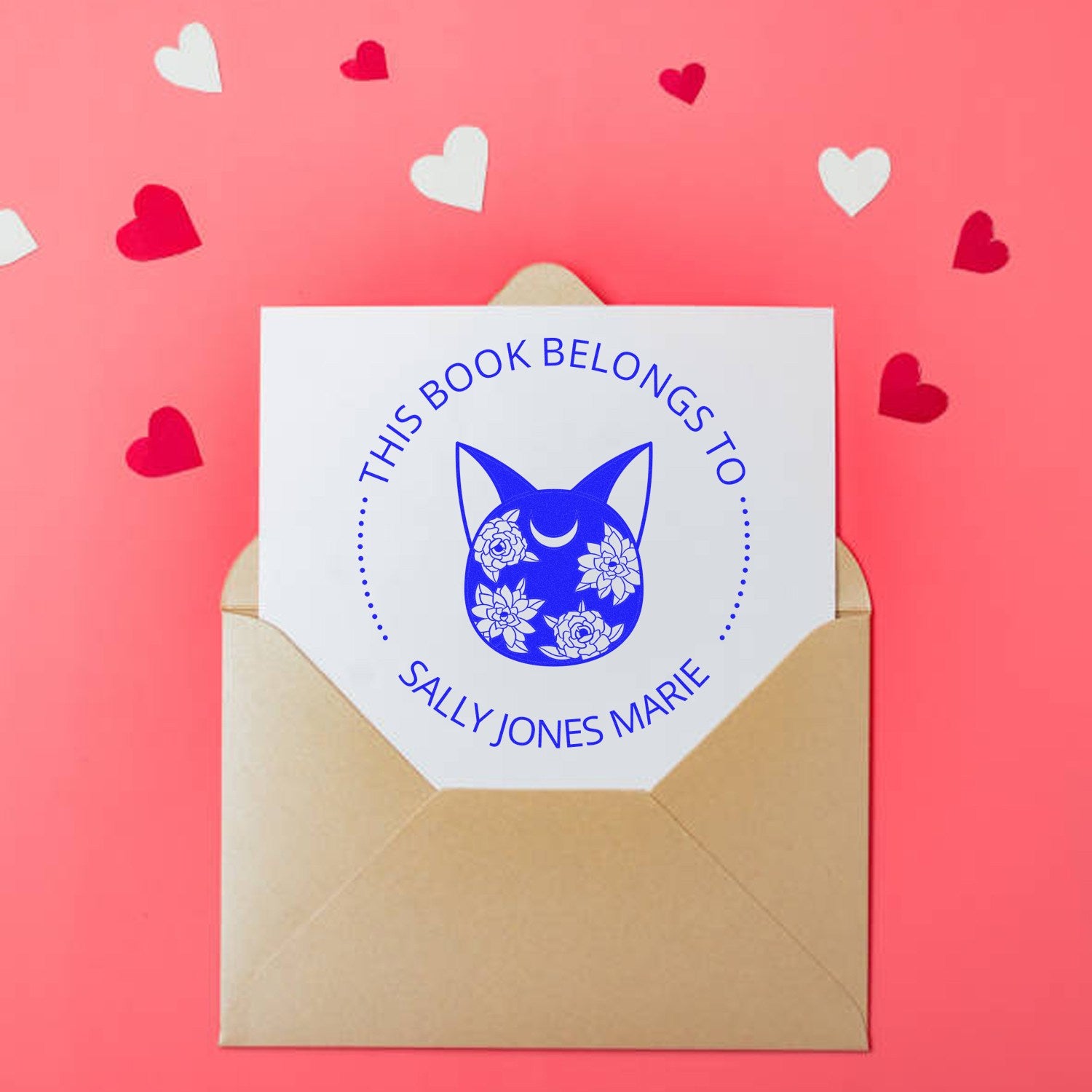 Custom blue stamp seal on tan envelope, with cat and floral design, on pink background with heart confetti.