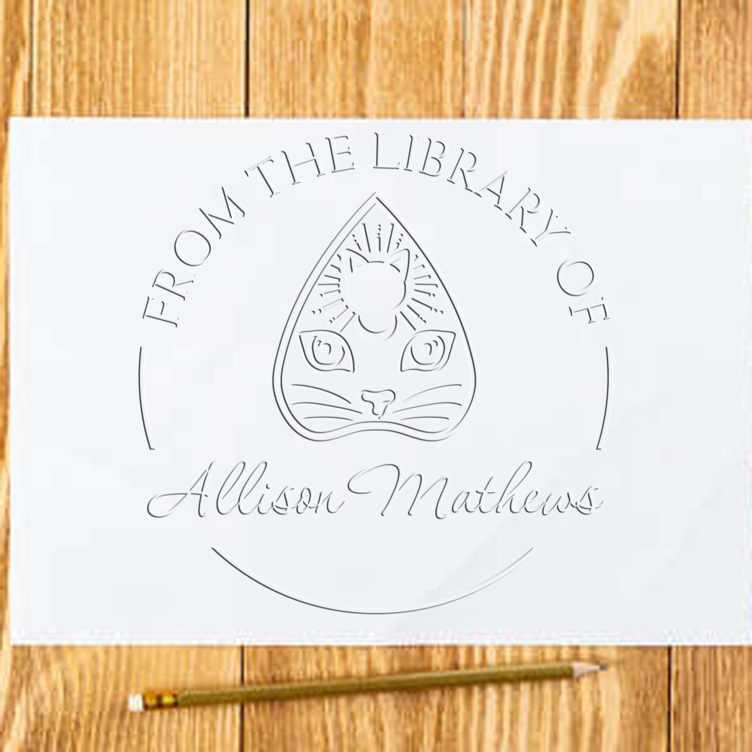 White embossed library stamp and seal with cat emblem and Allison Mathews text on a light wood background