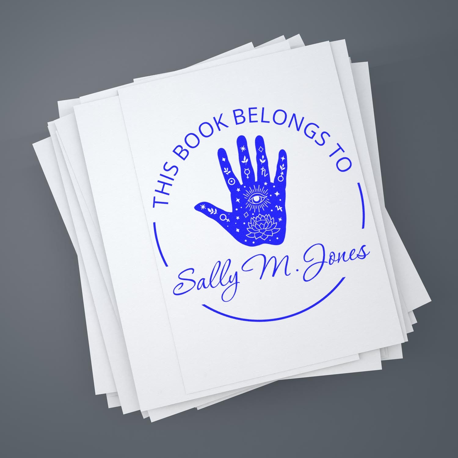 Blue custom book stamp seal on white papers, with hand emblem and This Book Belongs to Sally M. Jones text.