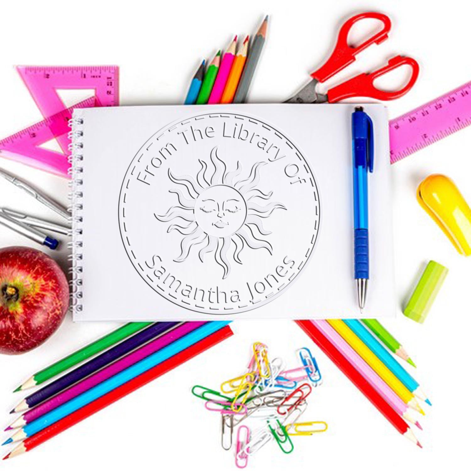 Custom library stamp and seal on white notebook, surrounded by colorful pencils, rulers, scissors, and pen.