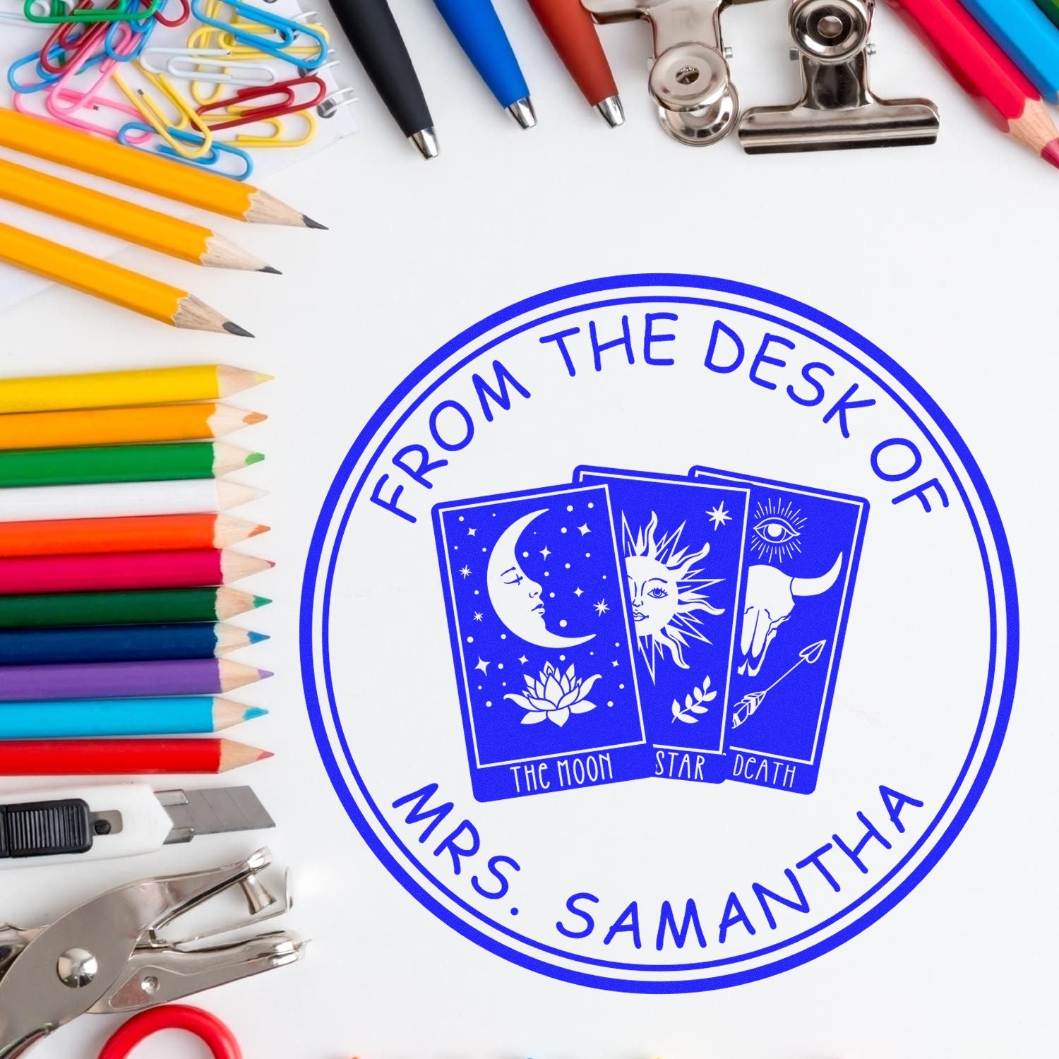 Round blue custom stamp seal for Mrs. Samantha with tarot cards, surrounded by colorful pencils, paper clips, and office tools.
