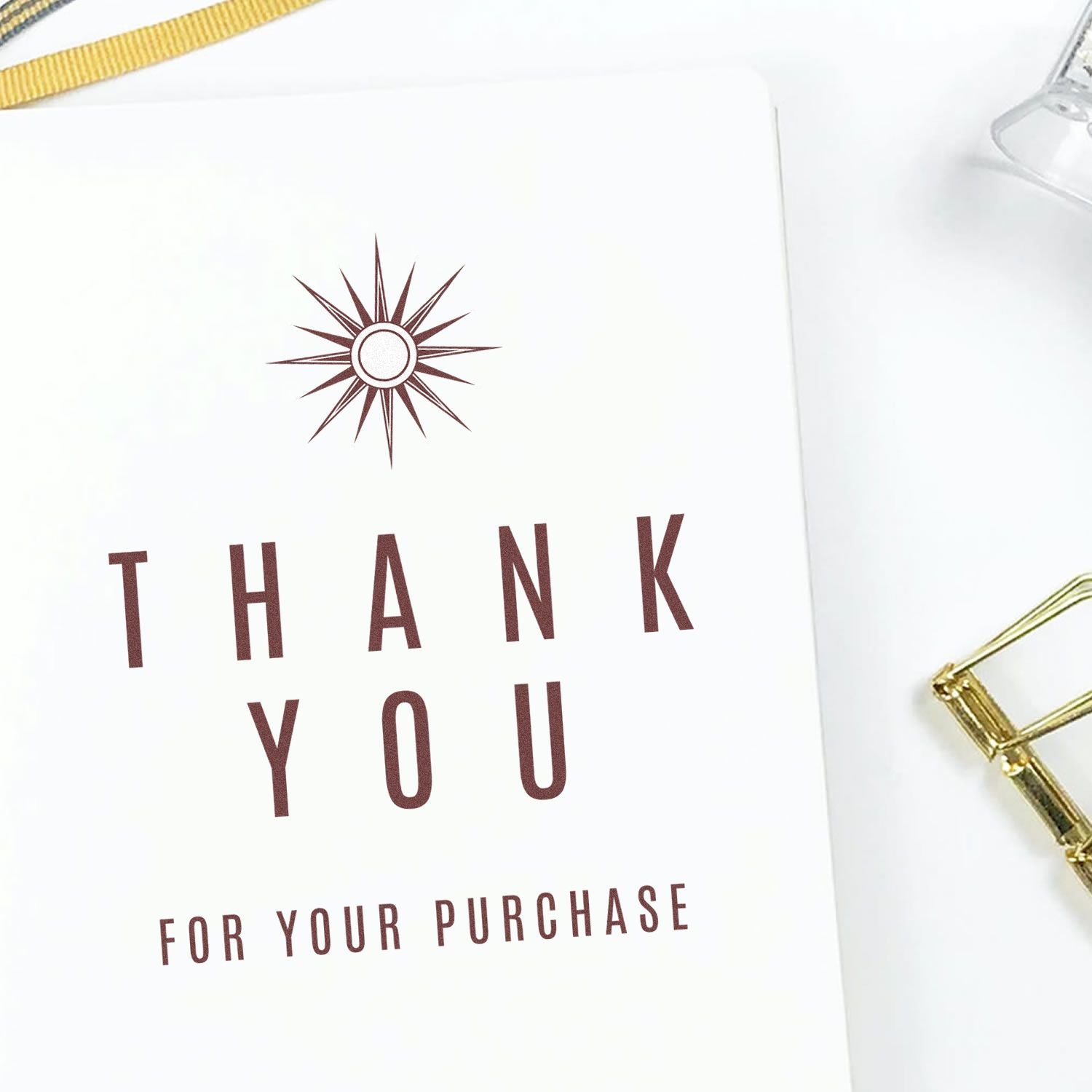 White thank-you card with burgundy starburst stamp seal, THANK YOU FOR YOUR PURCHASE text, and gold clip and ribbon accents.