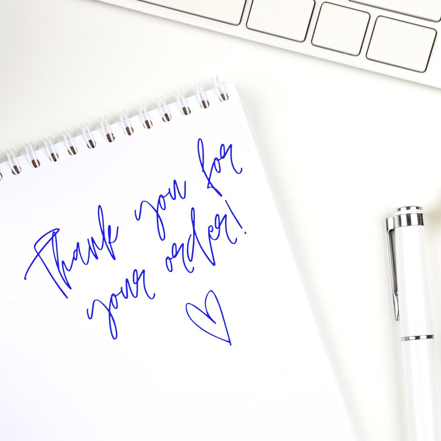 Blue thank-you stamp on white spiral notebook with heart, beside pen and keyboard; custom stamp and seal design.