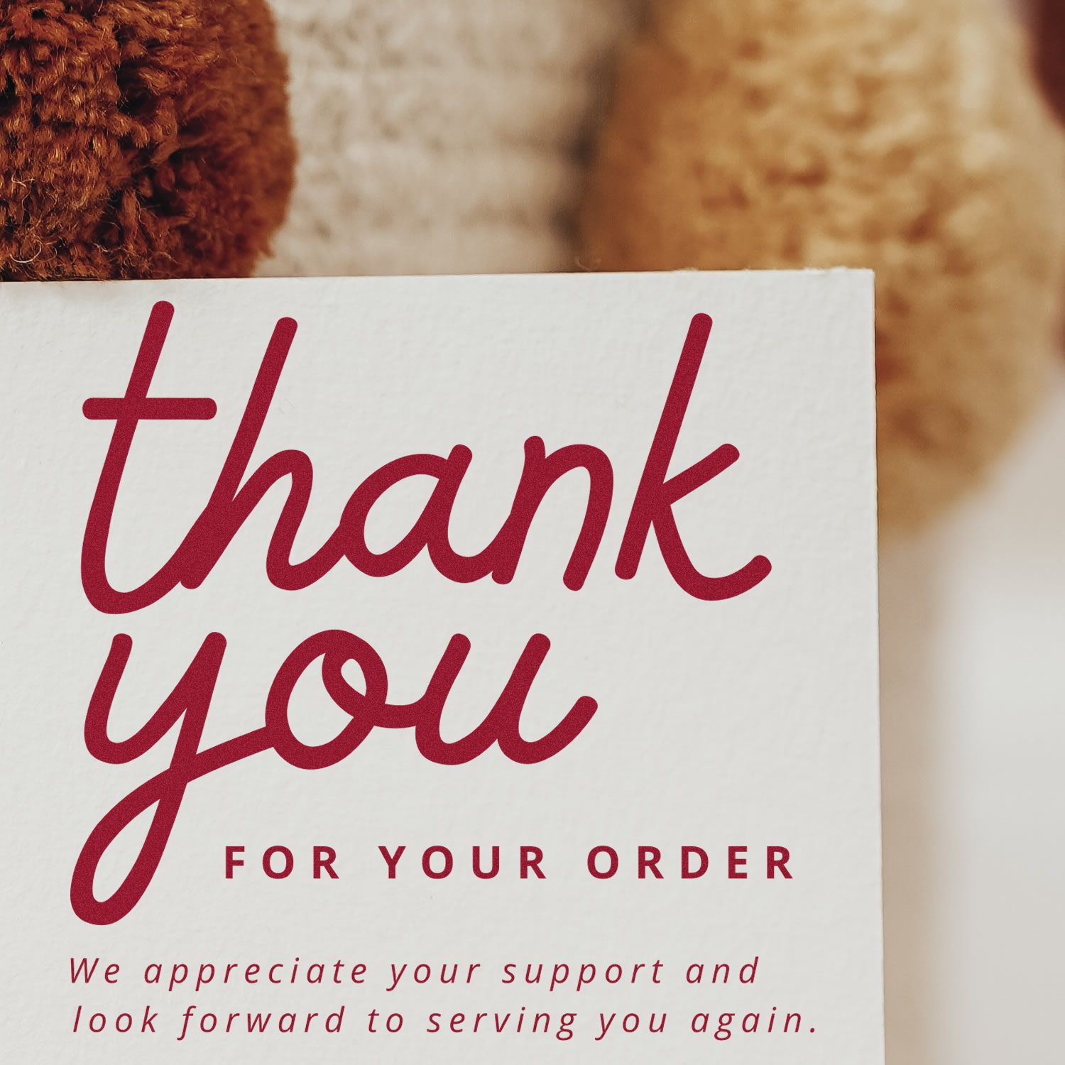 White thank-you card with red custom stamp/seal lettering, thank you for your order, on a warm brown blurred background.