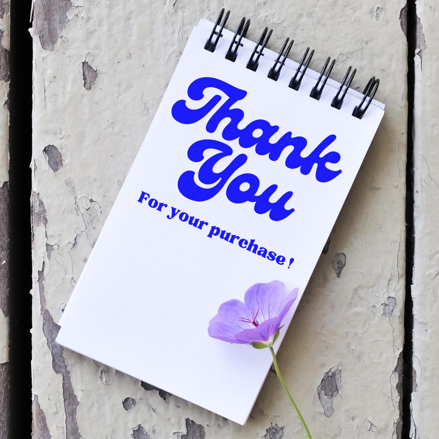 Custom blue thank-you stamp and seal on a white spiral notepad, with a purple flower on a distressed gray background.