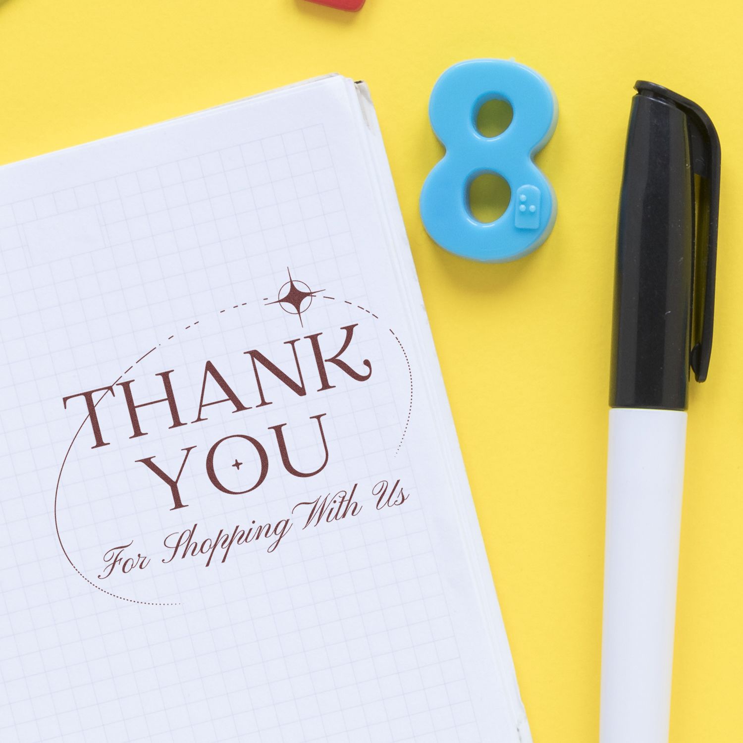 Brown thank-you seal stamped on a white grid notebook, with a blue number 8 seal and black marker on a bright yellow background.