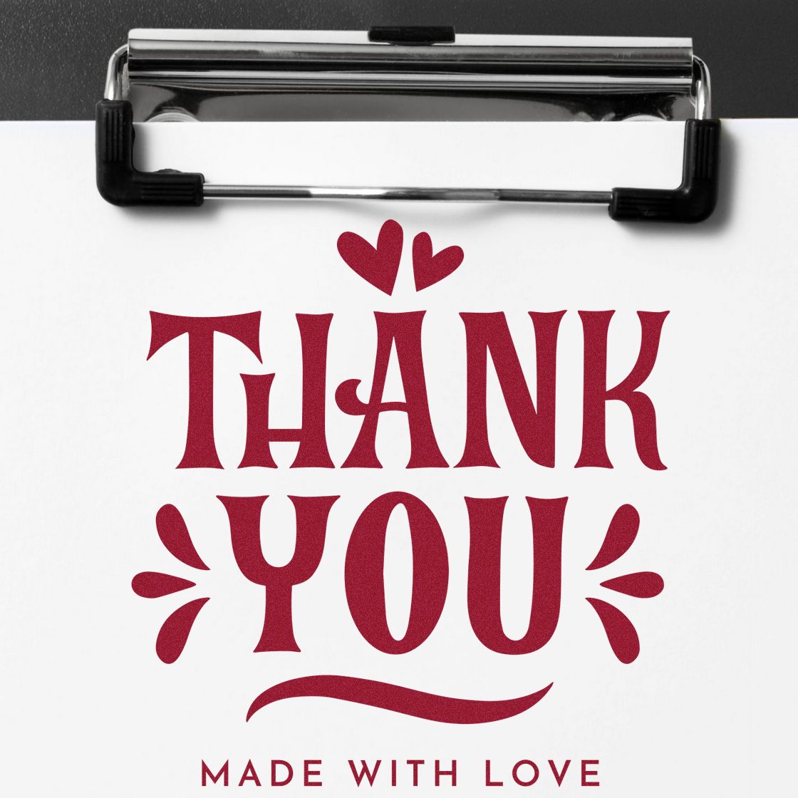 Red thank-you stamp with hearts and Made with Love on white paper, clipped to a black seal-stamp clipboard.