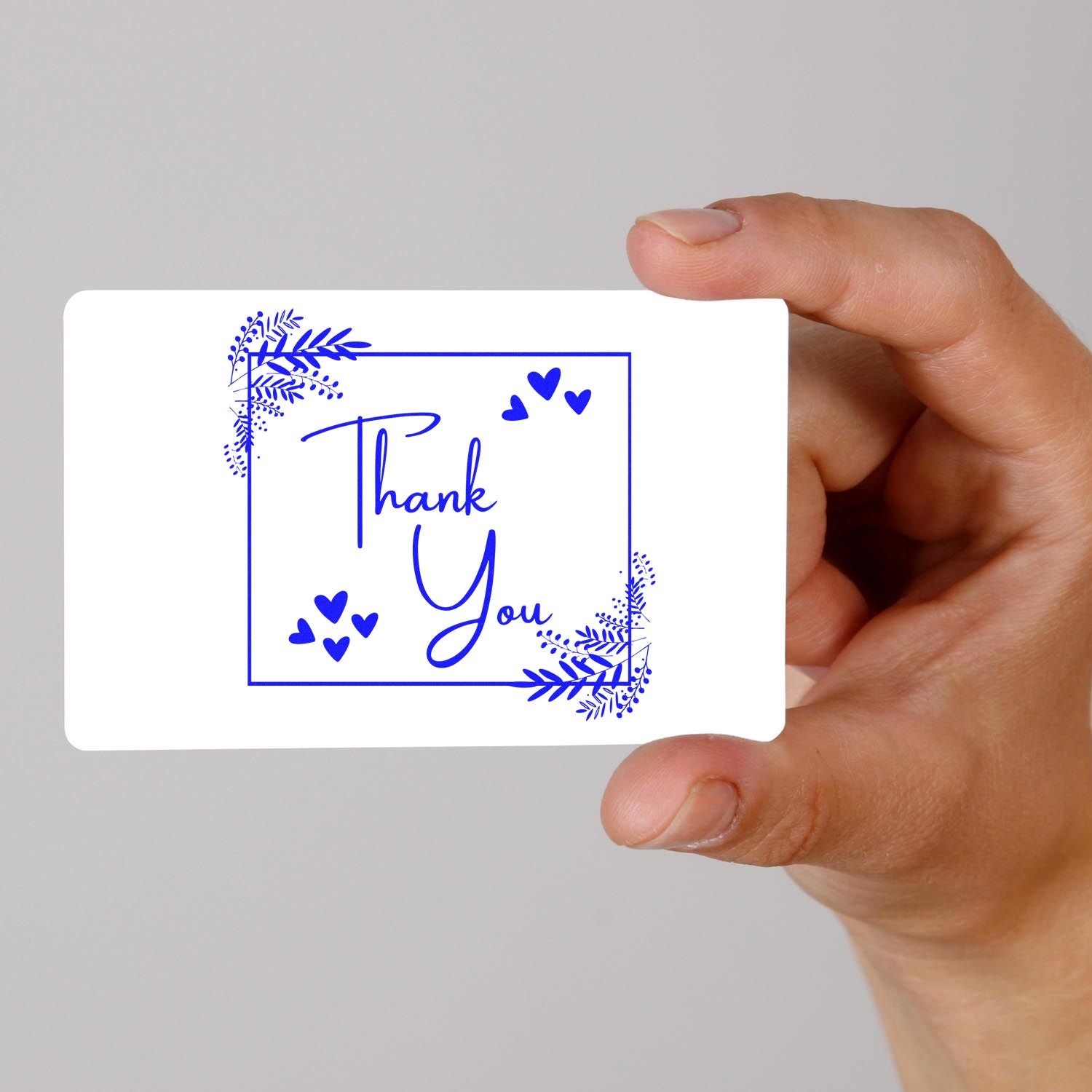 Blue Thank You stamp seal card with hearts and floral corners, held by hand on a white background.