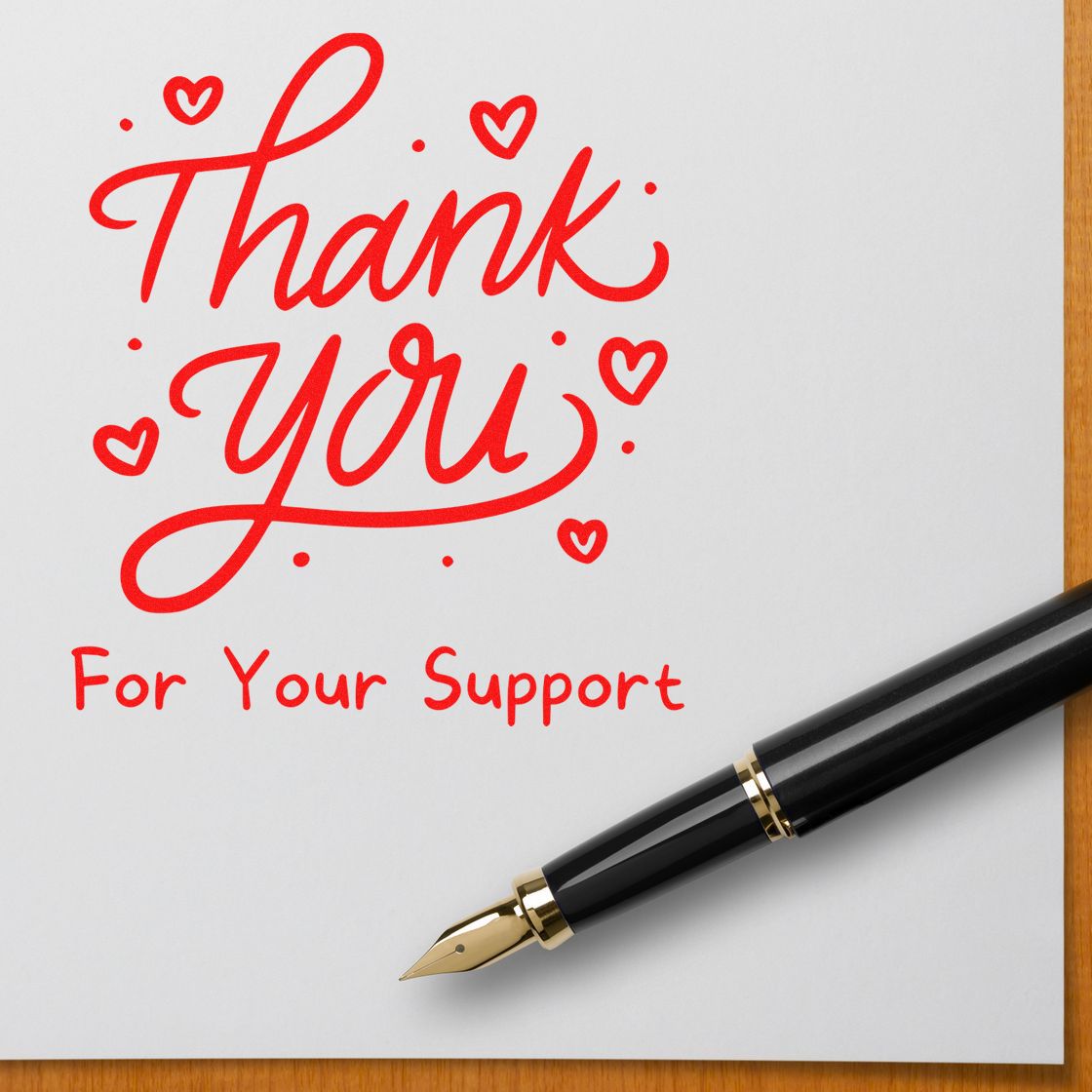 Red thank-you stamp and seal with hearts on white paper, beside a black-and-gold fountain pen.