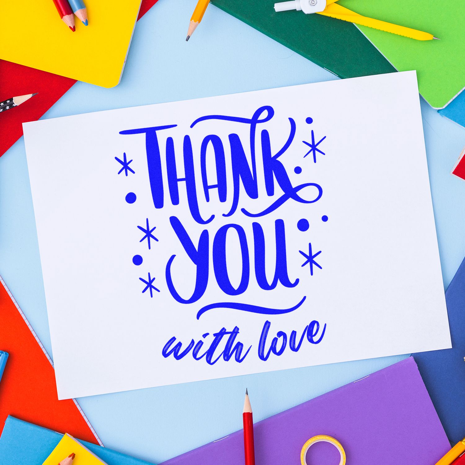 Blue thank-you stamp and seal on a white card, surrounded by colorful notebooks and pencils.
