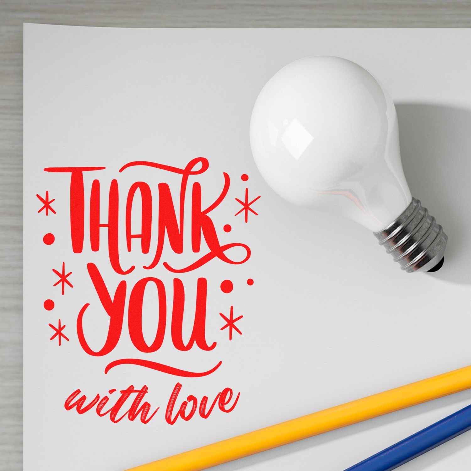 Red Thank You with love stamp/seal design on white paper with a white light bulb and yellow-blue pencils.