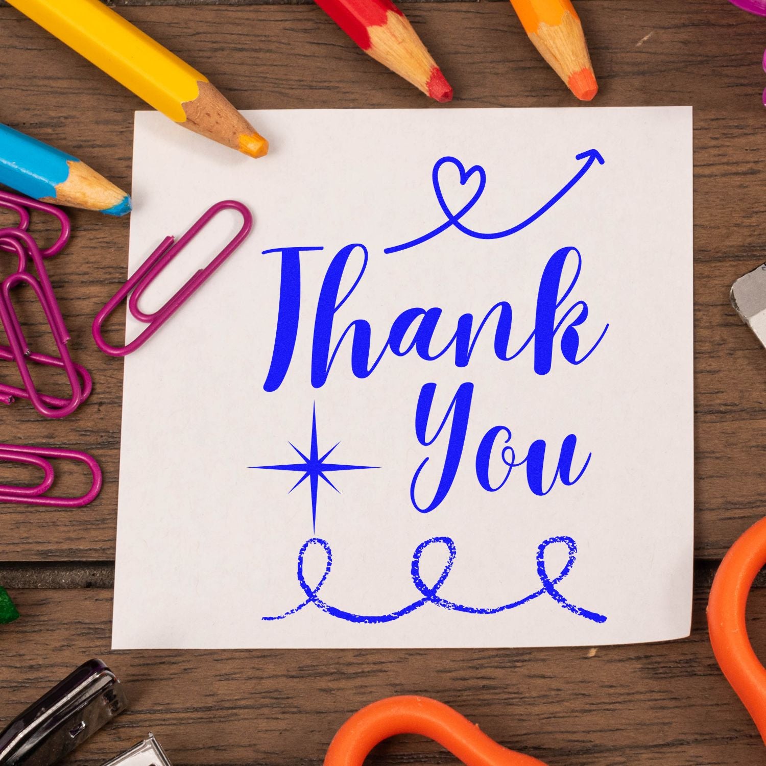 Blue Thank You stamp and seal on white card, surrounded by colorful pencils and magenta paper clips on a wood desk.