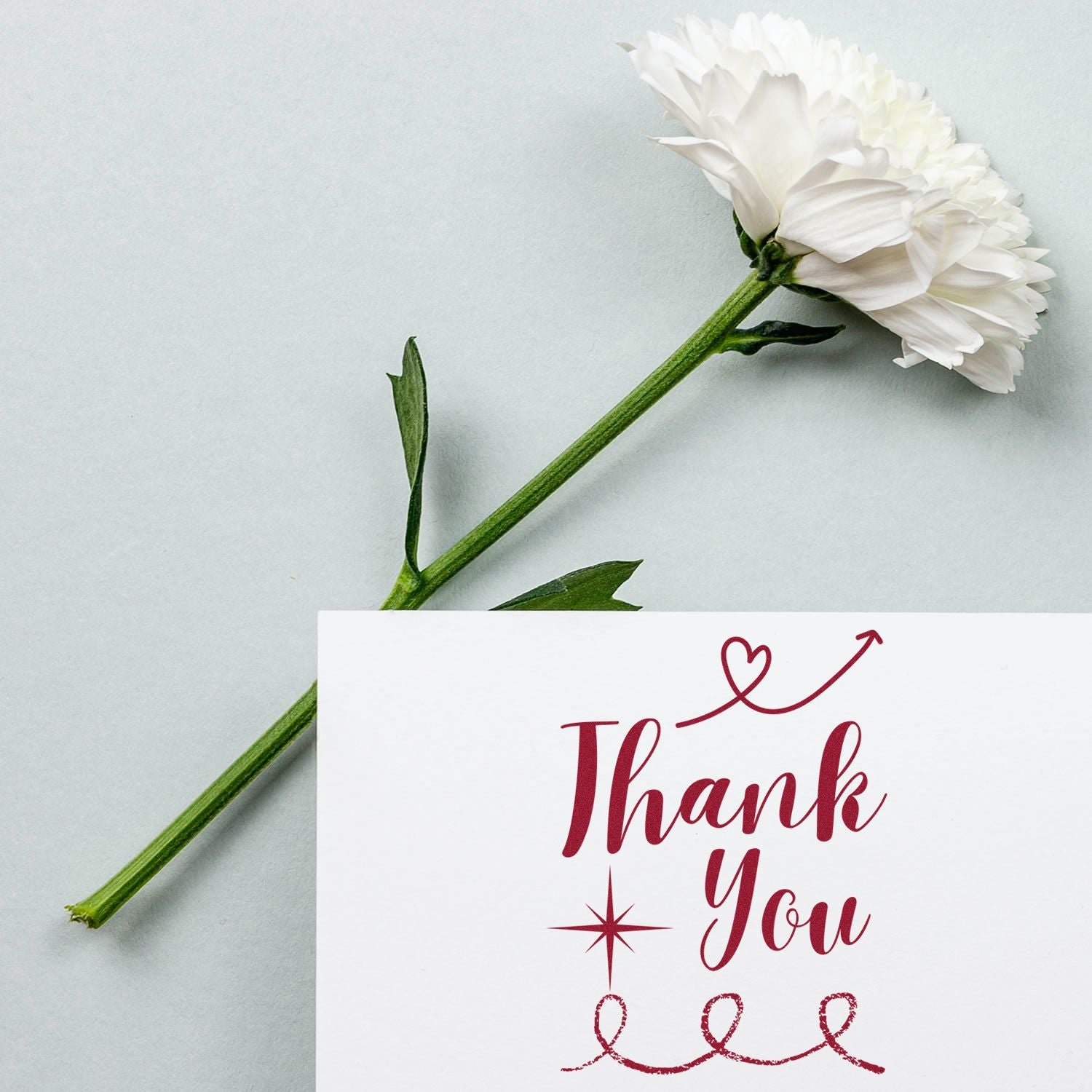 White flower beside a maroon Thank You stamp and seal design on a white card, with heart and star accents.
