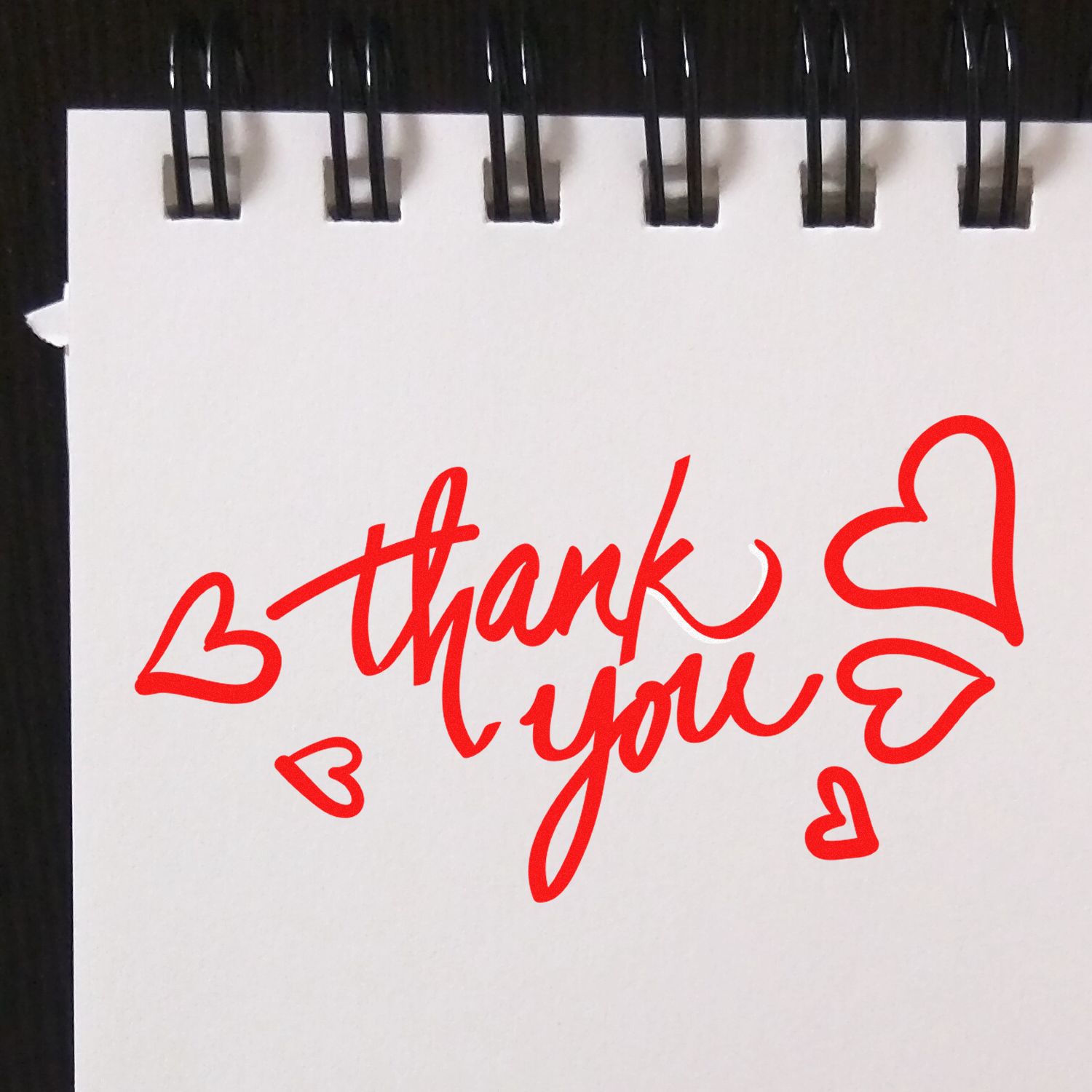 Red thank-you stamp design with heart accents on a white spiral notebook page for stamp and seal products.