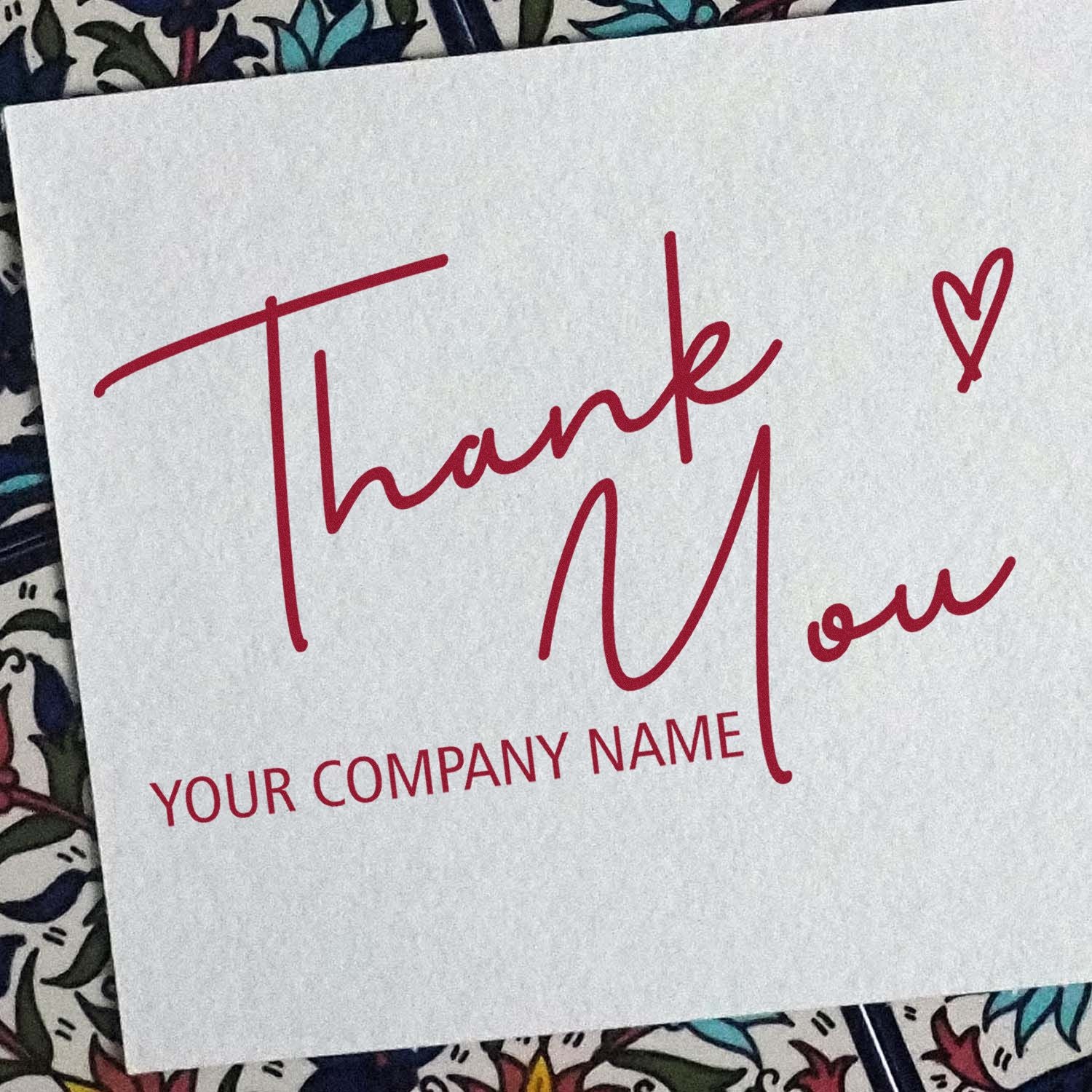 Red custom thank-you stamp and seal on white card with heart and company name, over patterned fabric.