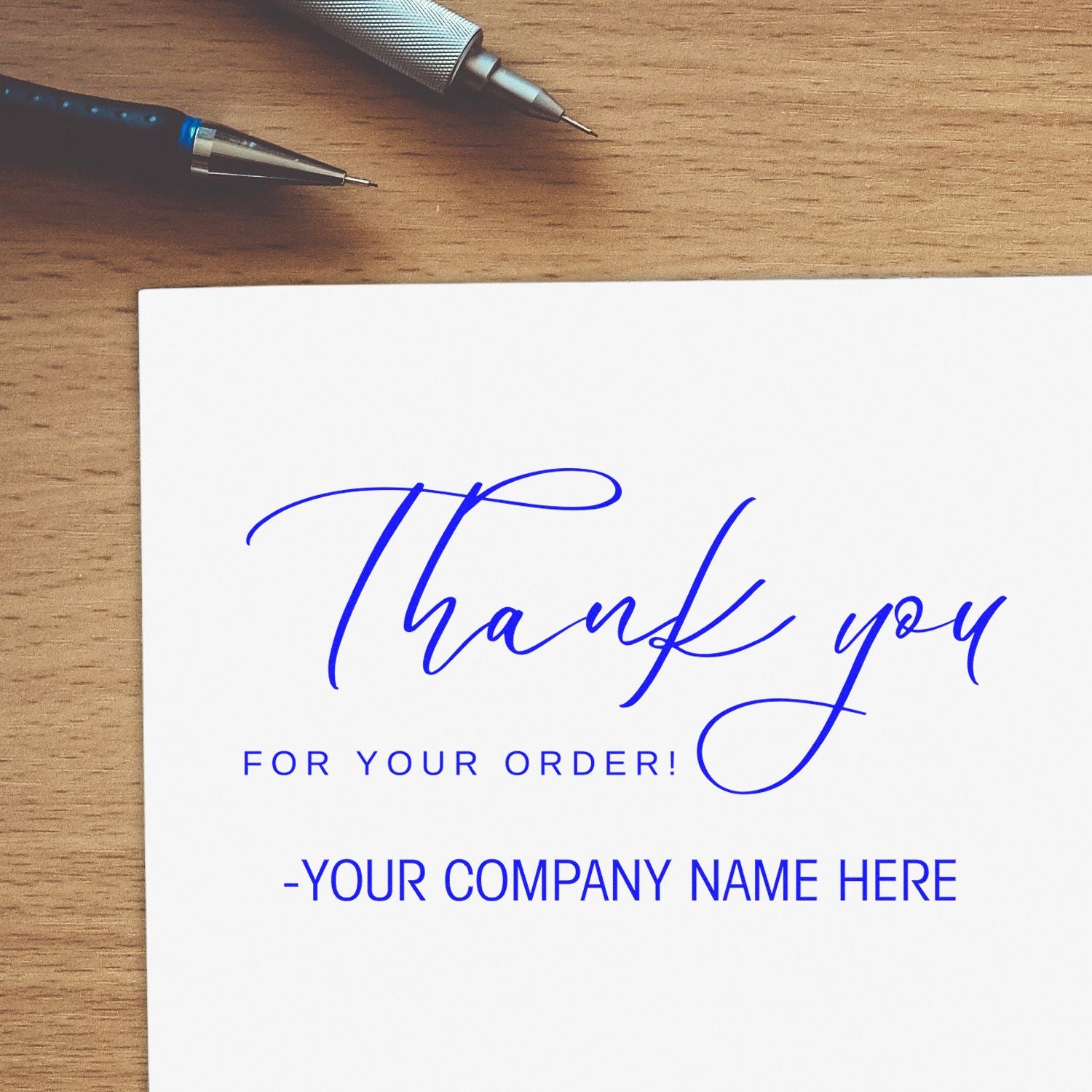 Blue custom stamp and seal sample reading Thank you for your order! on white paper with pens on a wood desk.