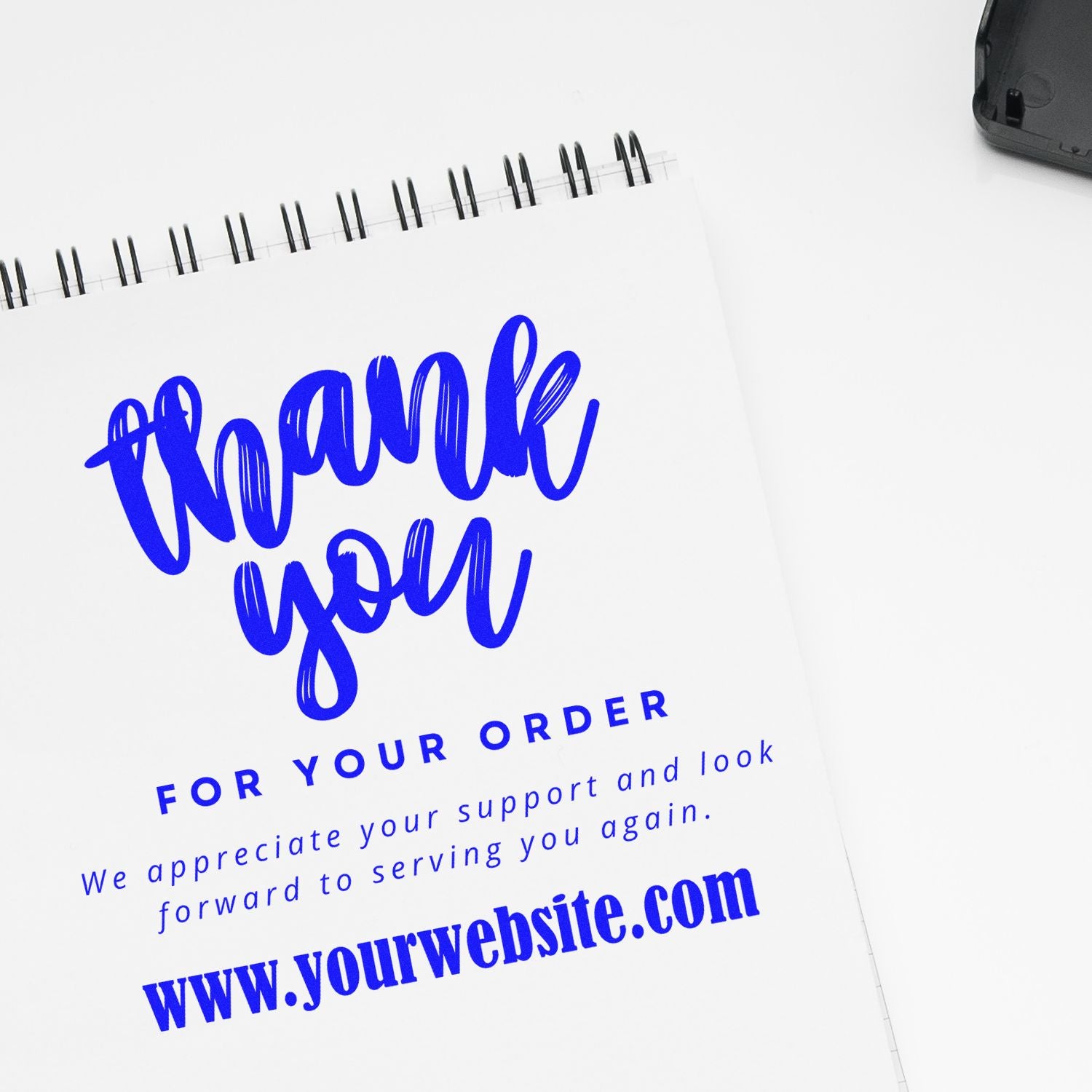 Blue custom stamp and seal sample on spiral notebook with Thank you for your order and website text on white background.