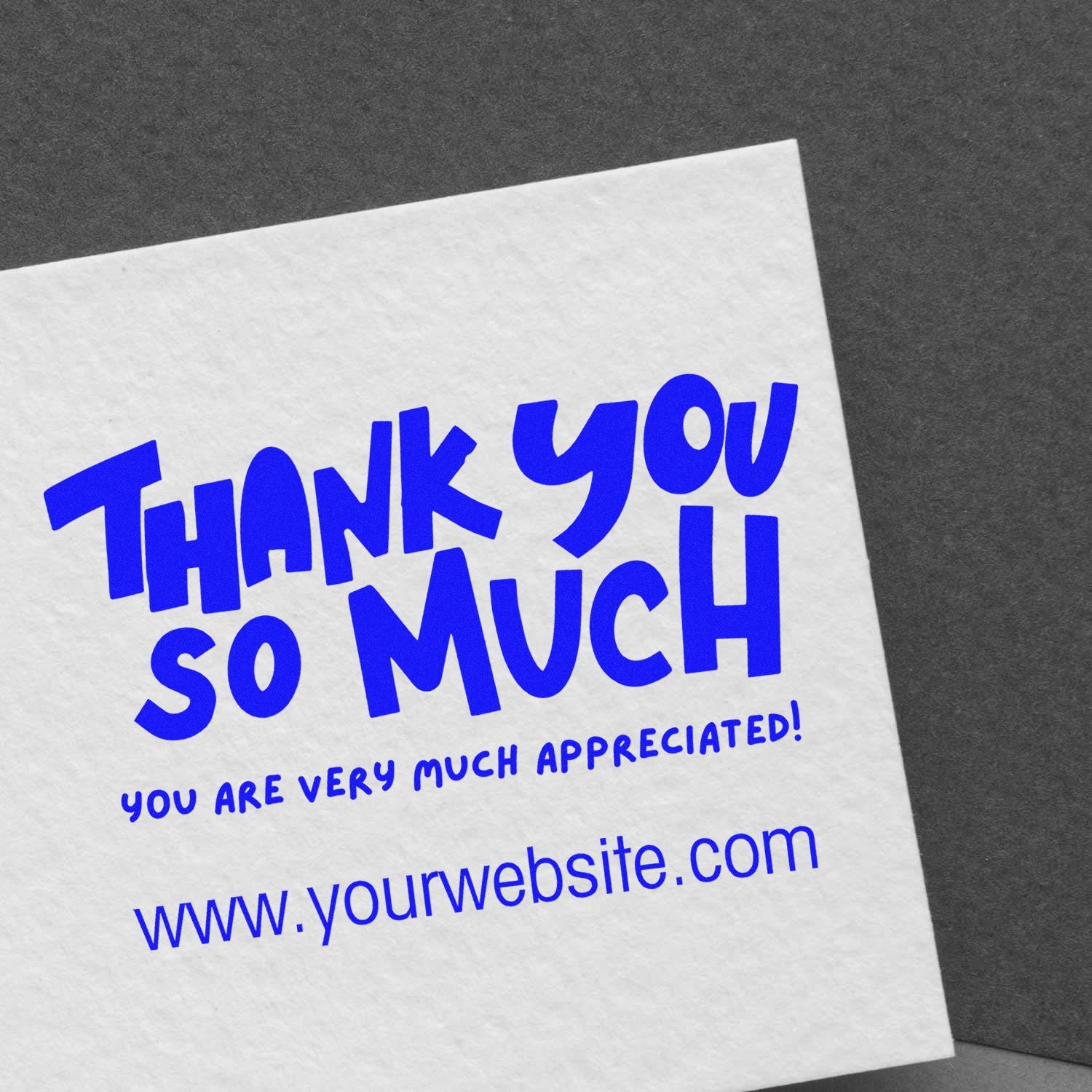 Blue custom thank-you stamp and seal on white paper with website, set against a dark gray background.