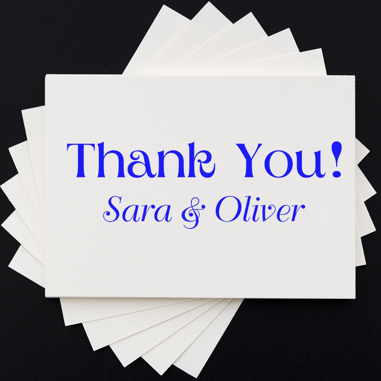 Stacked white thank-you cards with blue custom stamp and seal text reading Thank You! Sara & Oliver on a black background.